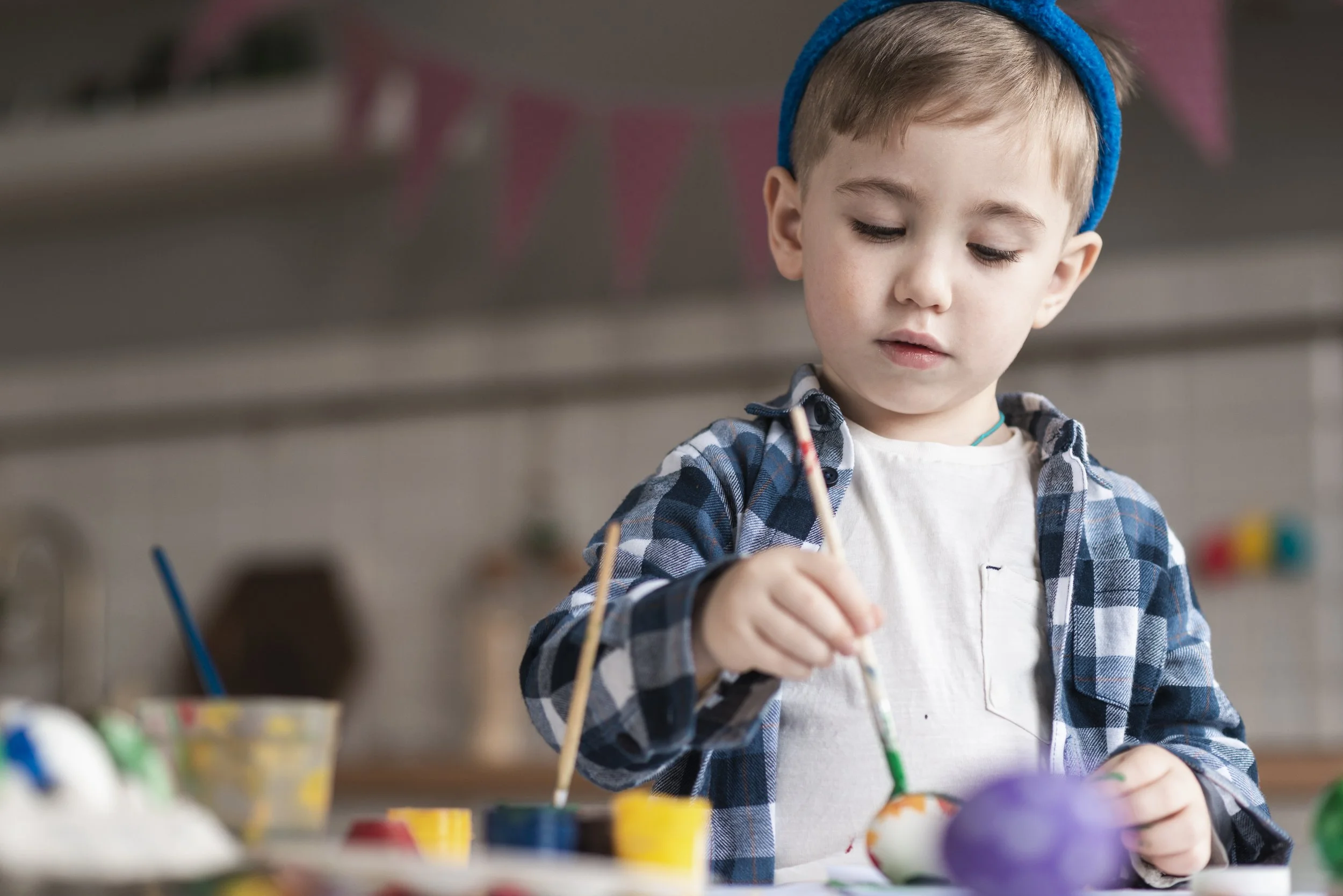 Young boy painting decorated eggs at a table in a kitchen for Easter.