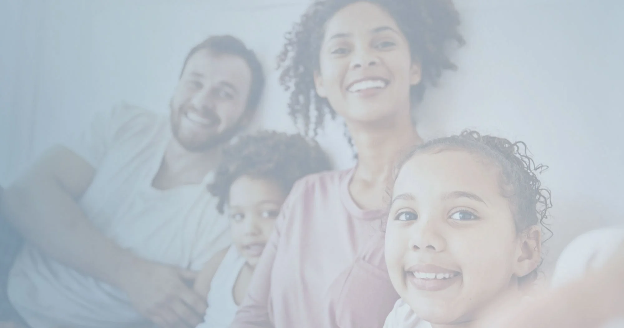 A family of four smiling together in a brightly lit room. The group includes a man, a woman, and two children.