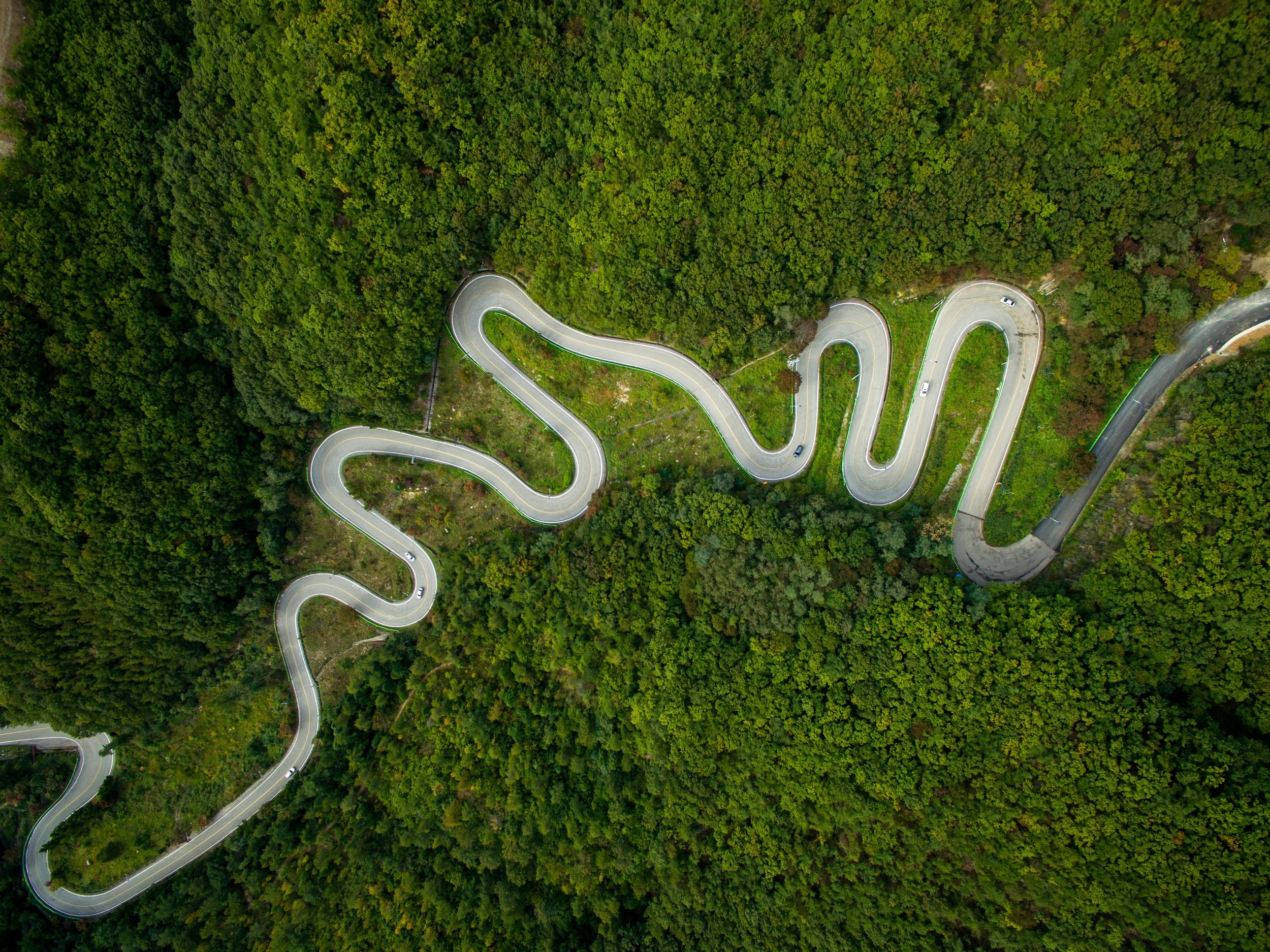 An aerial view of a winding mountain road through a dense green forest.