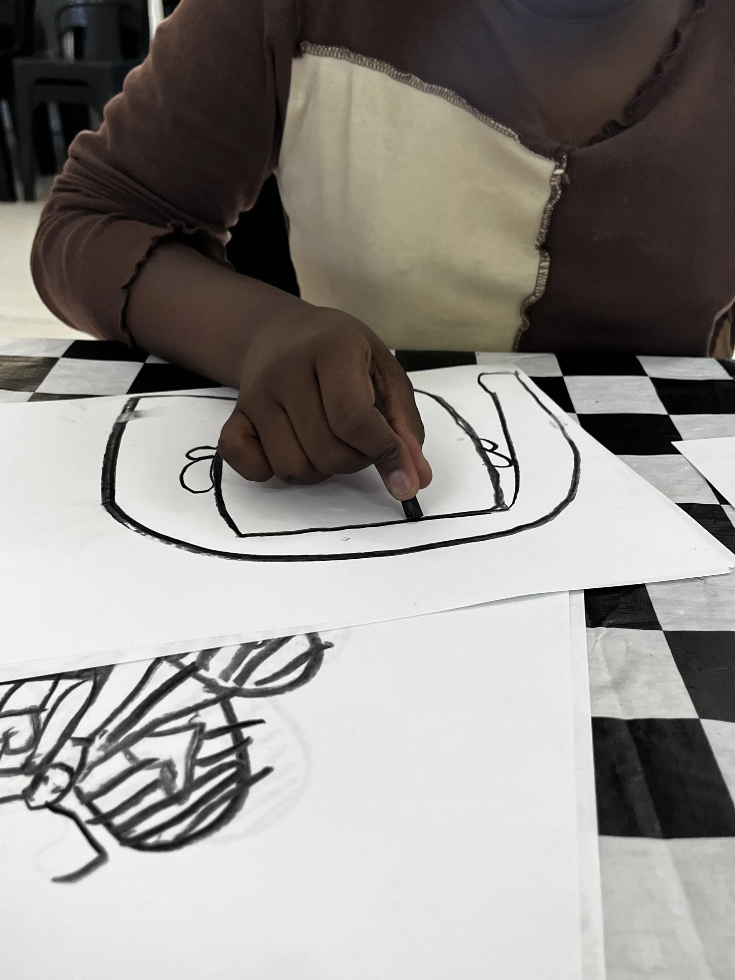 Person drawing a caricature on paper, with unfinished caricature of a person with glasses and curly hair visible.