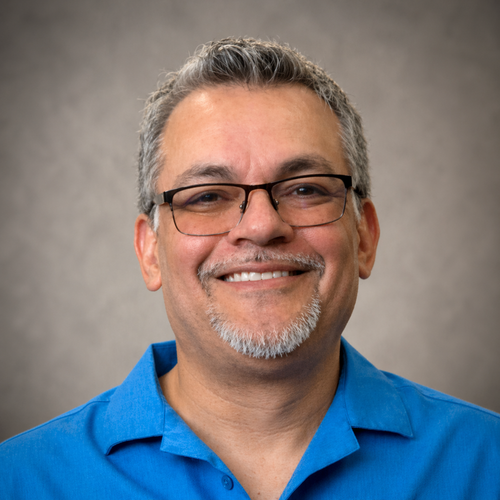Professional headshot of Maurice Rico, print specialist offering business cards, banners, photos, brochures, cards, and stickers. Blue shirt, wearing glasses.