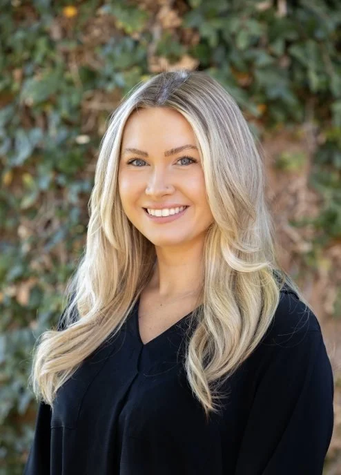 BNI Community Connectors, Arizona, Anna Sperbeck with long blonde hair, smiling, wearing a black top outdoors with green foliage in the background.