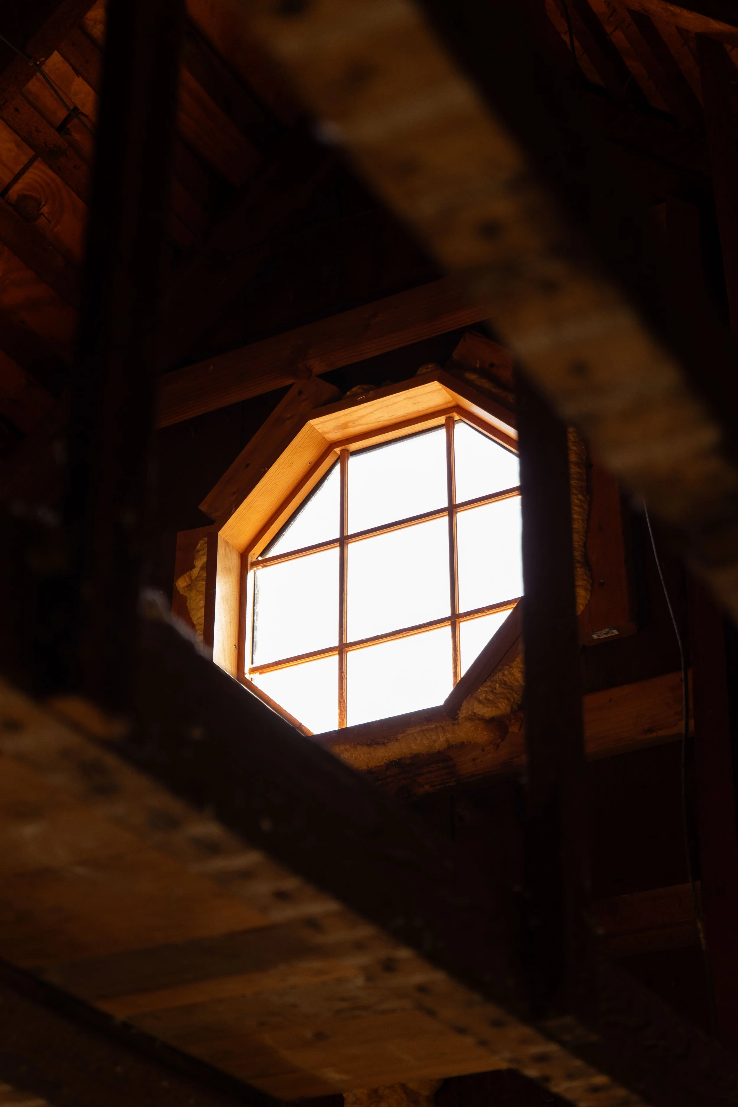Octagonal attic window framed by wooden beams — architectural detail photo by DRiccardi Photography, Long Island NY.