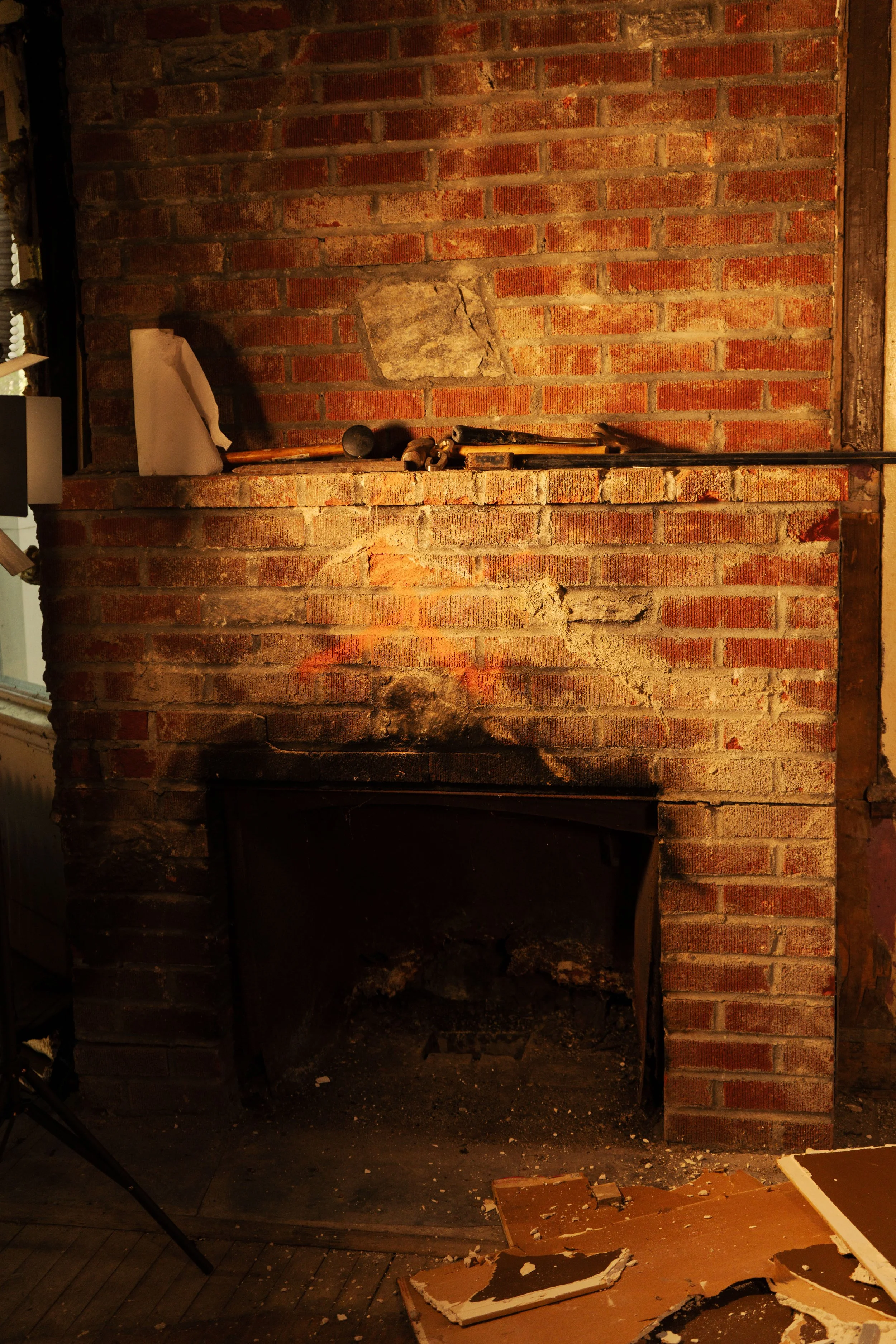 Old brick fireplace with tools and debris in golden light — architectural decay photography by DRiccardi Photography.
