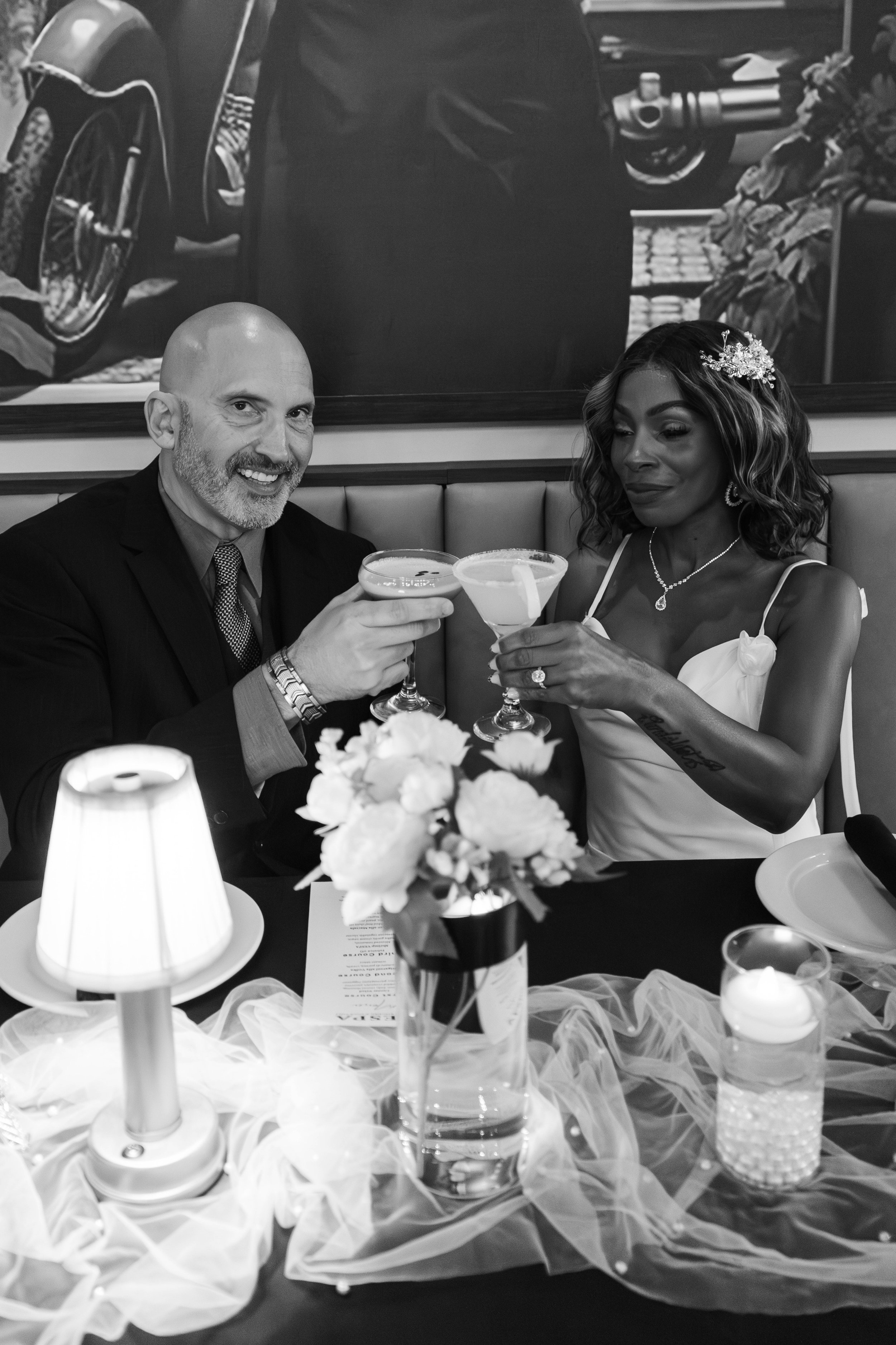 Black and white photo of couple toasting with cocktails at dinner table — engagement photography by DRiccardi Photography, Long Island NY.