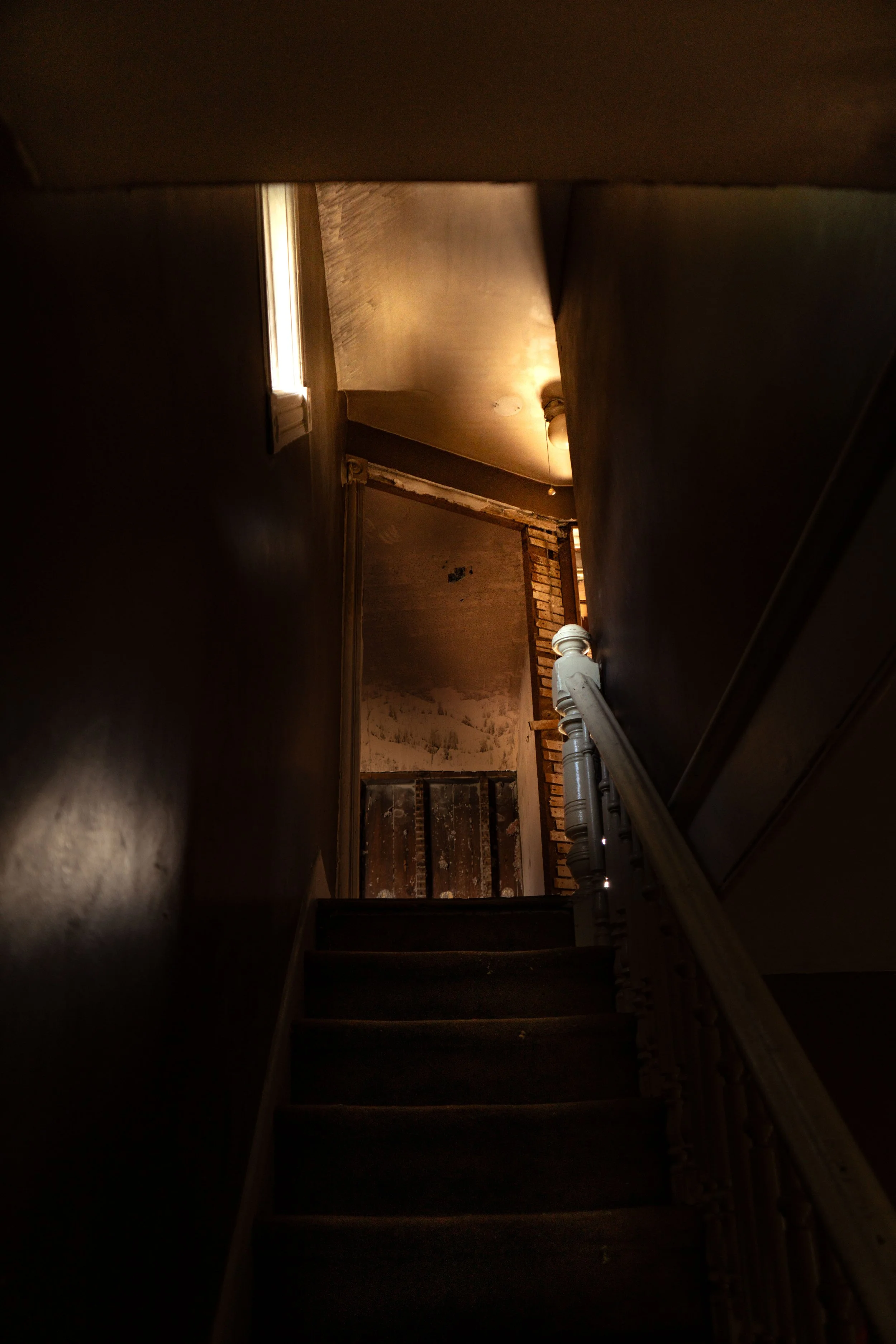 Dimly lit staircase leading upward into unfinished hallway — moody architectural photograph by DRiccardi Photography, Long Island.