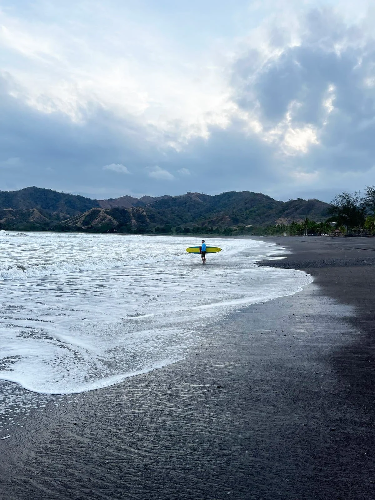 surfer standing on the beach at Guanico Beach Resort admiring the break