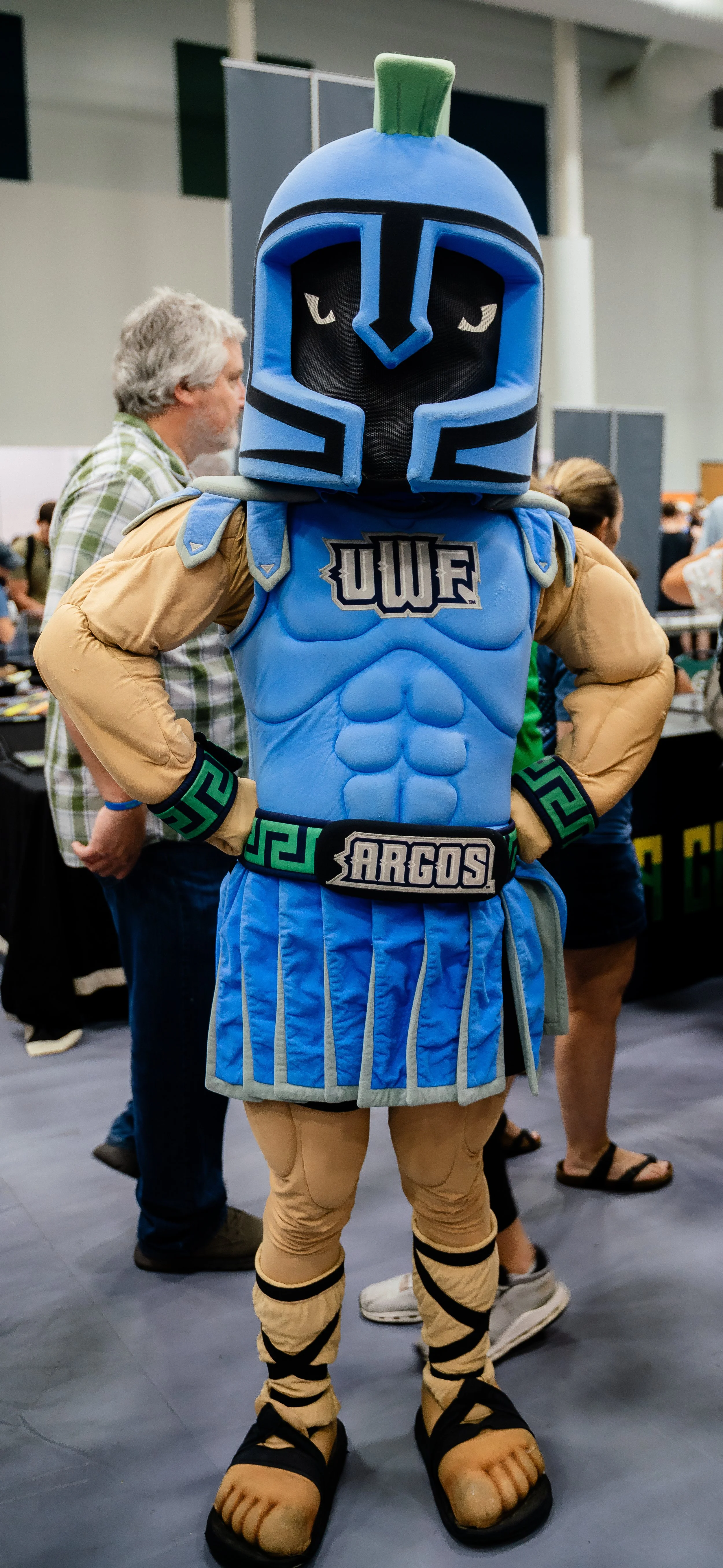 Costumed character dressed as an armored warrior with blue and black helmet, muscular torso, and animal paws, wearing themed shorts and belt, at a convention.