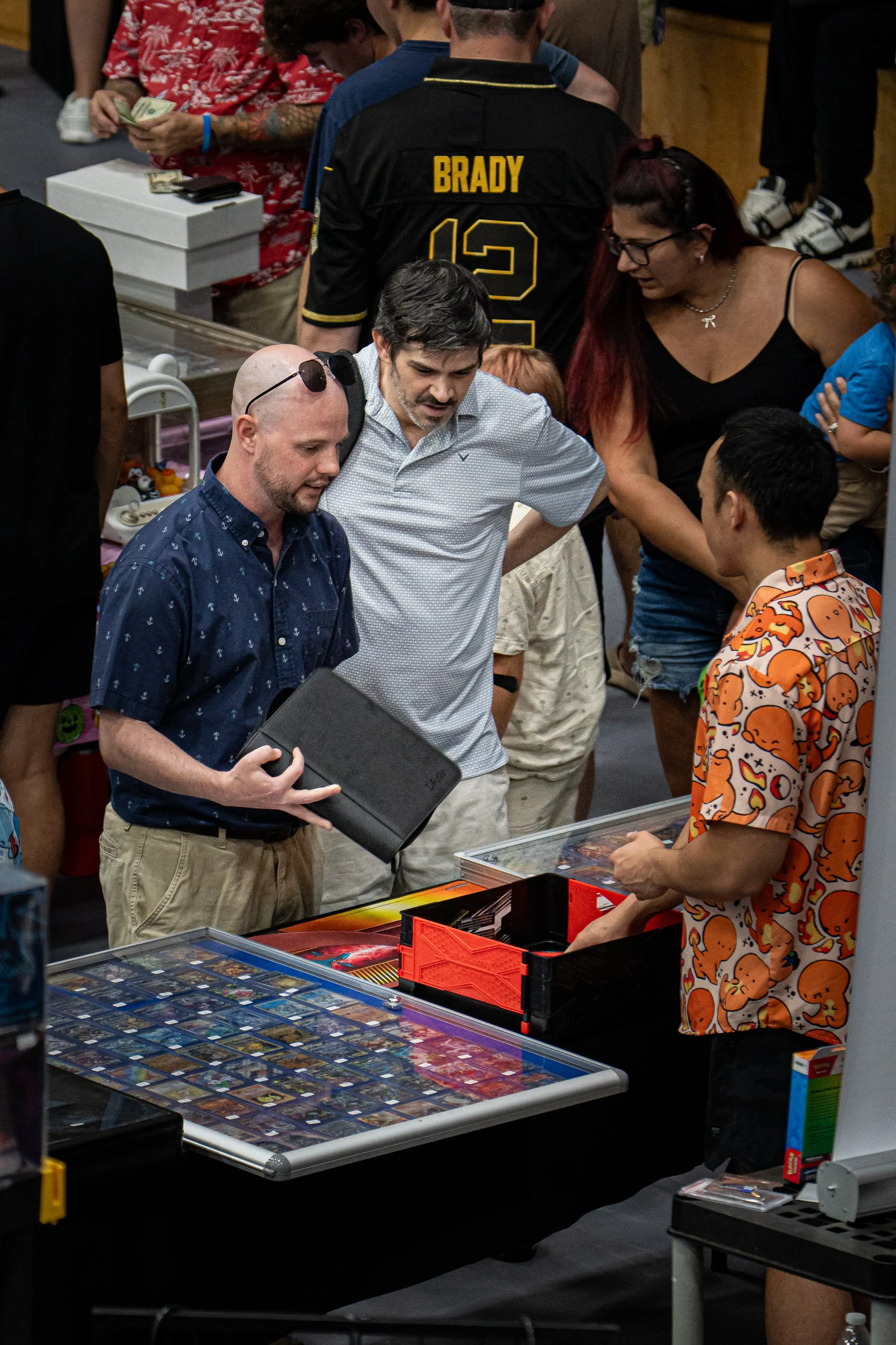 People shopping for trading cards at a store, with one person in a black jersey with the name 'Brady' and the number 12.