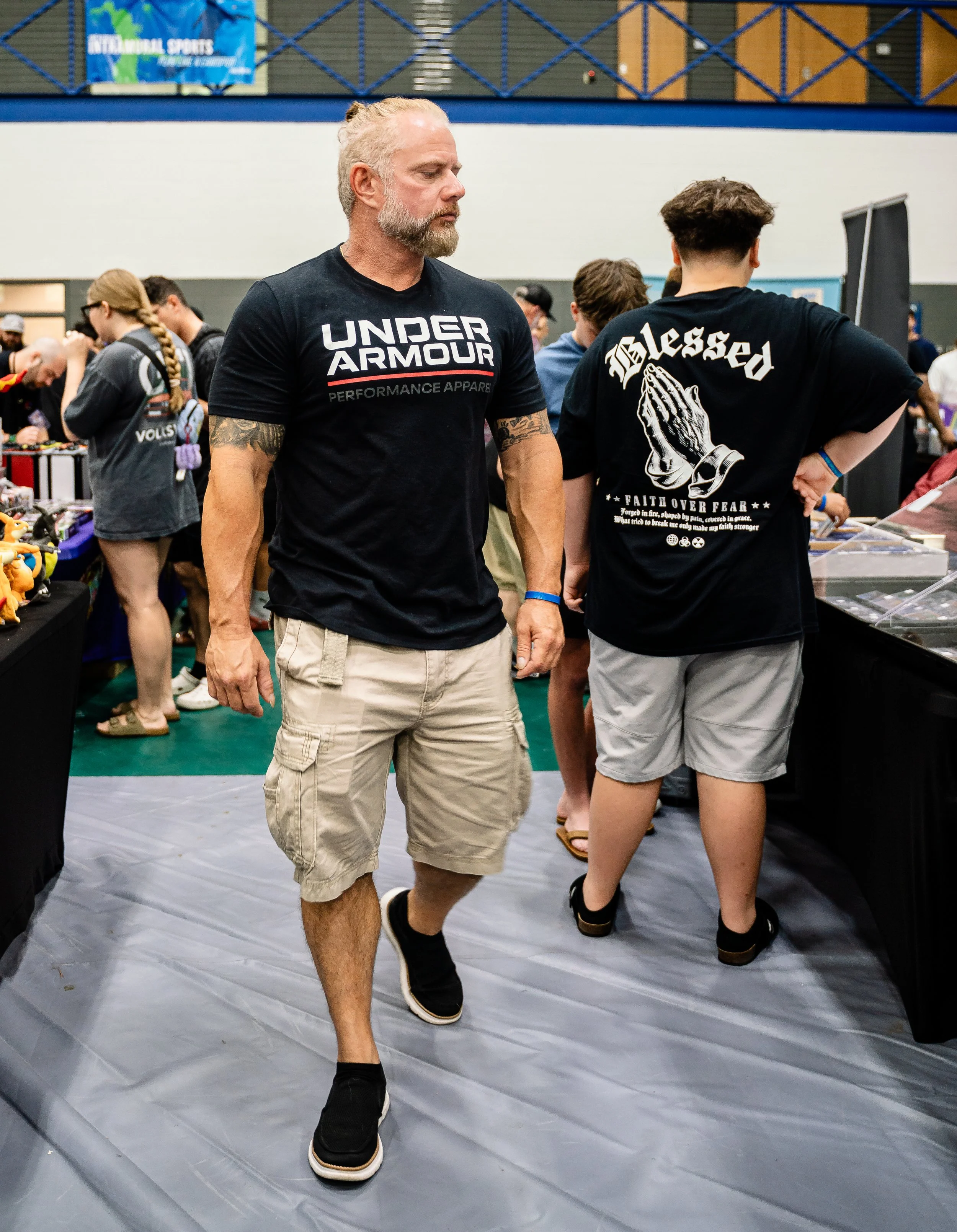 People browsing at an indoor artificial sports or trading event, with tables of merchandise and a sign in the background.