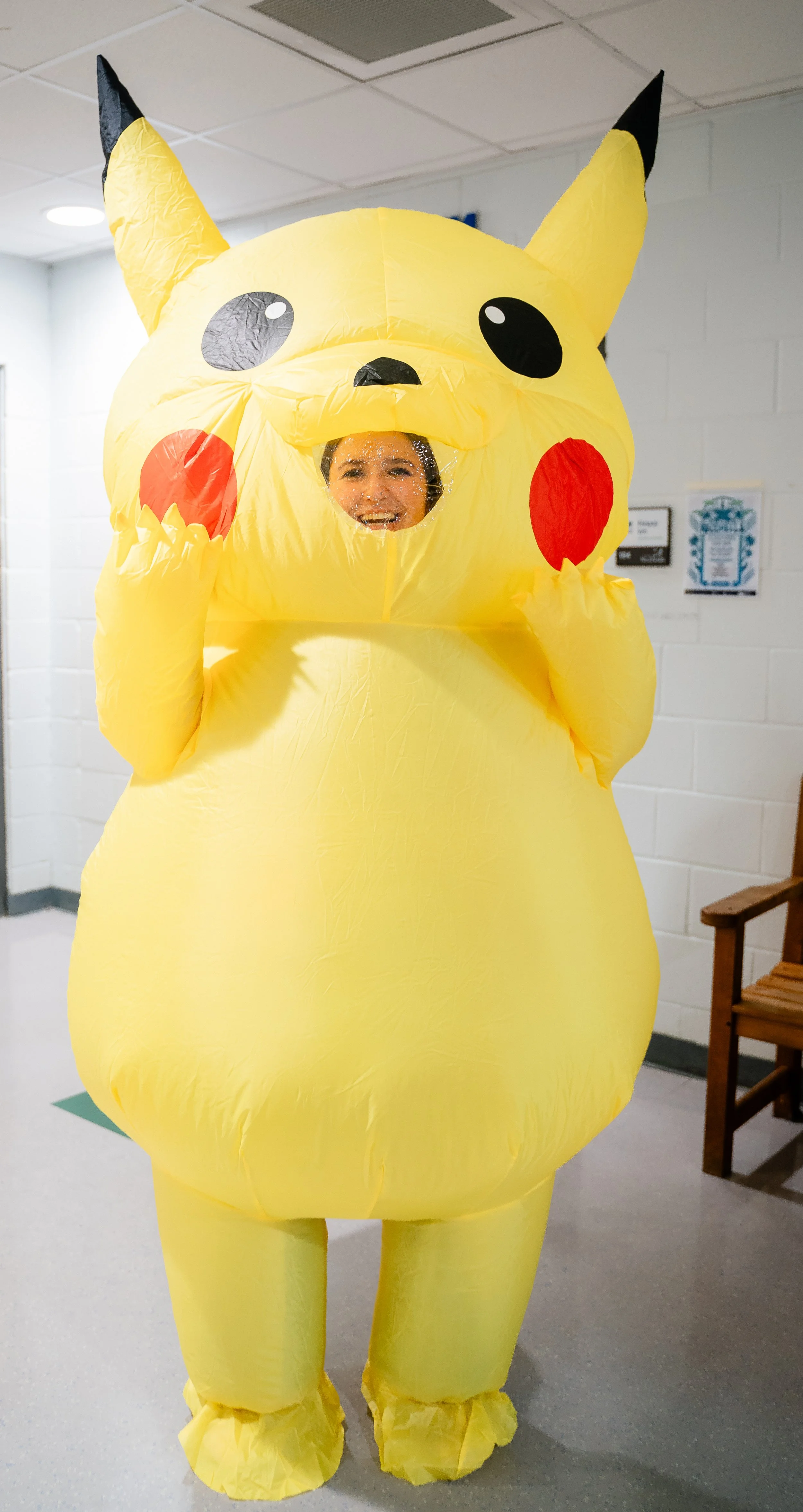 Person in Pikachu costume standing indoors in front of white brick walls.