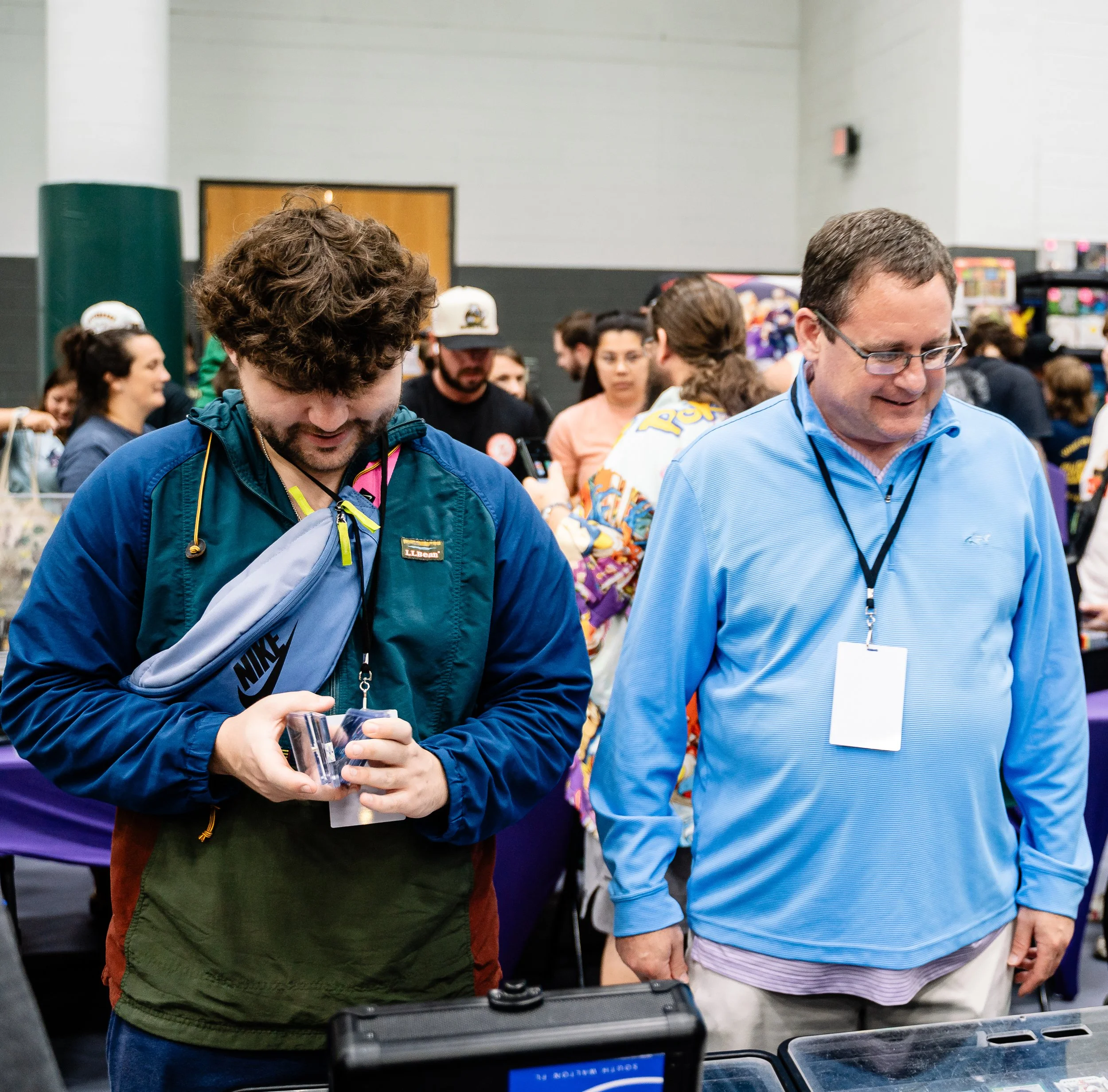 People gathered in an indoor space, possibly at a convention or event, with some smiling and engaging with items on a table.