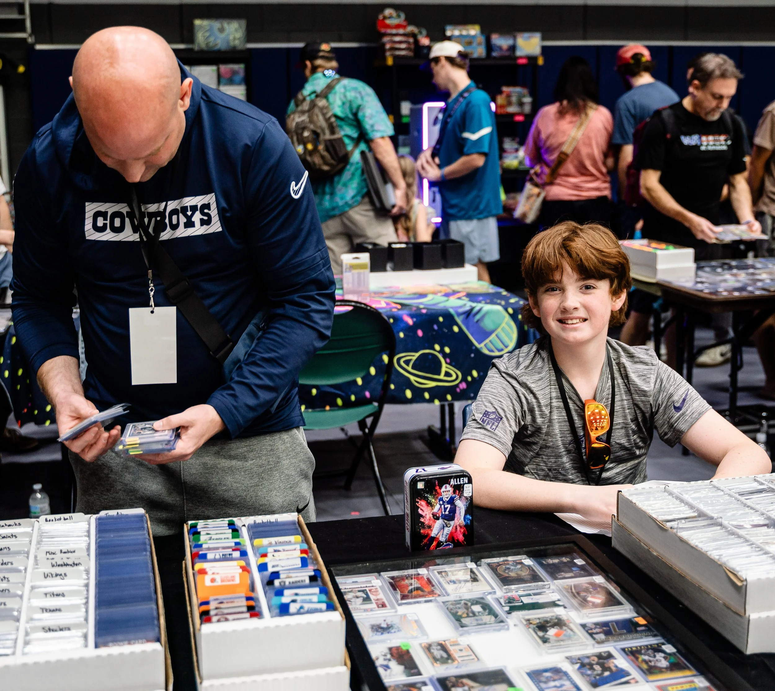 People browsing collectible cards and sports memorabilia at an indoor trading event.