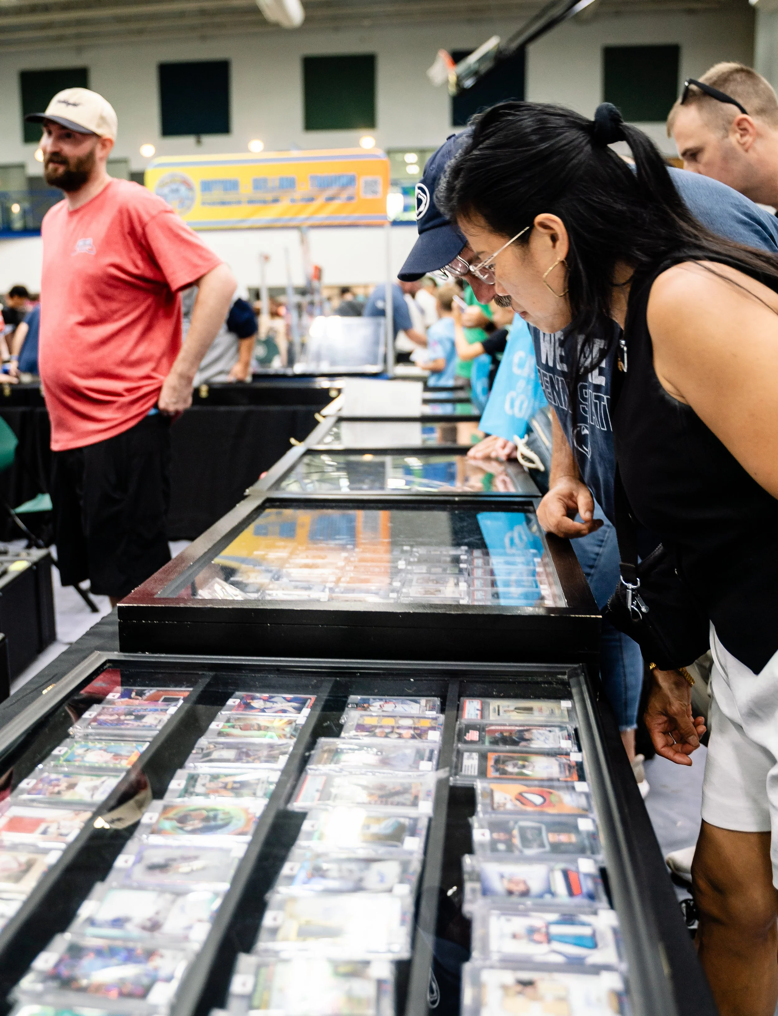 People browsing sports cards and memorabilia behind glass display cases at a convention or store.