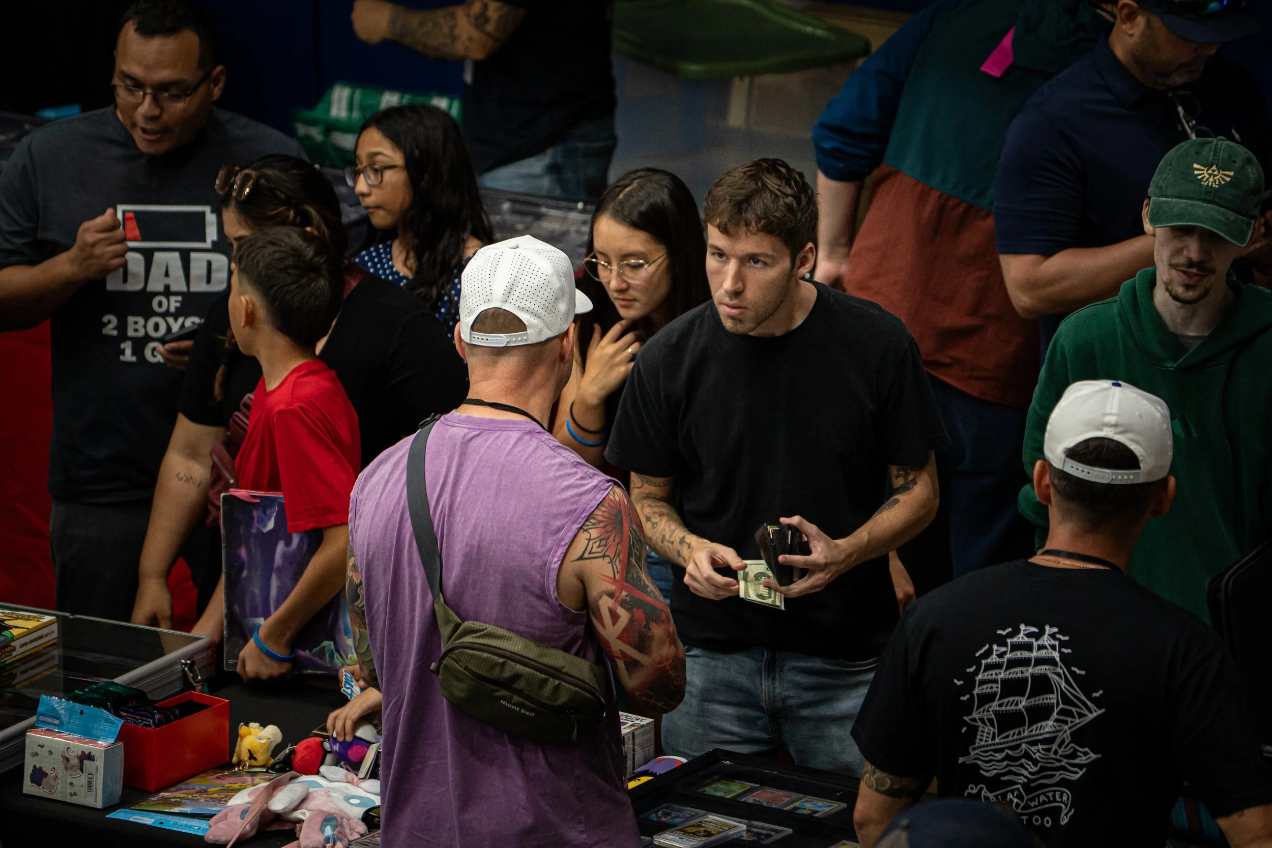 People shopping at a booth with toys and collectibles, some engaging in conversation, inside a crowded indoor market.