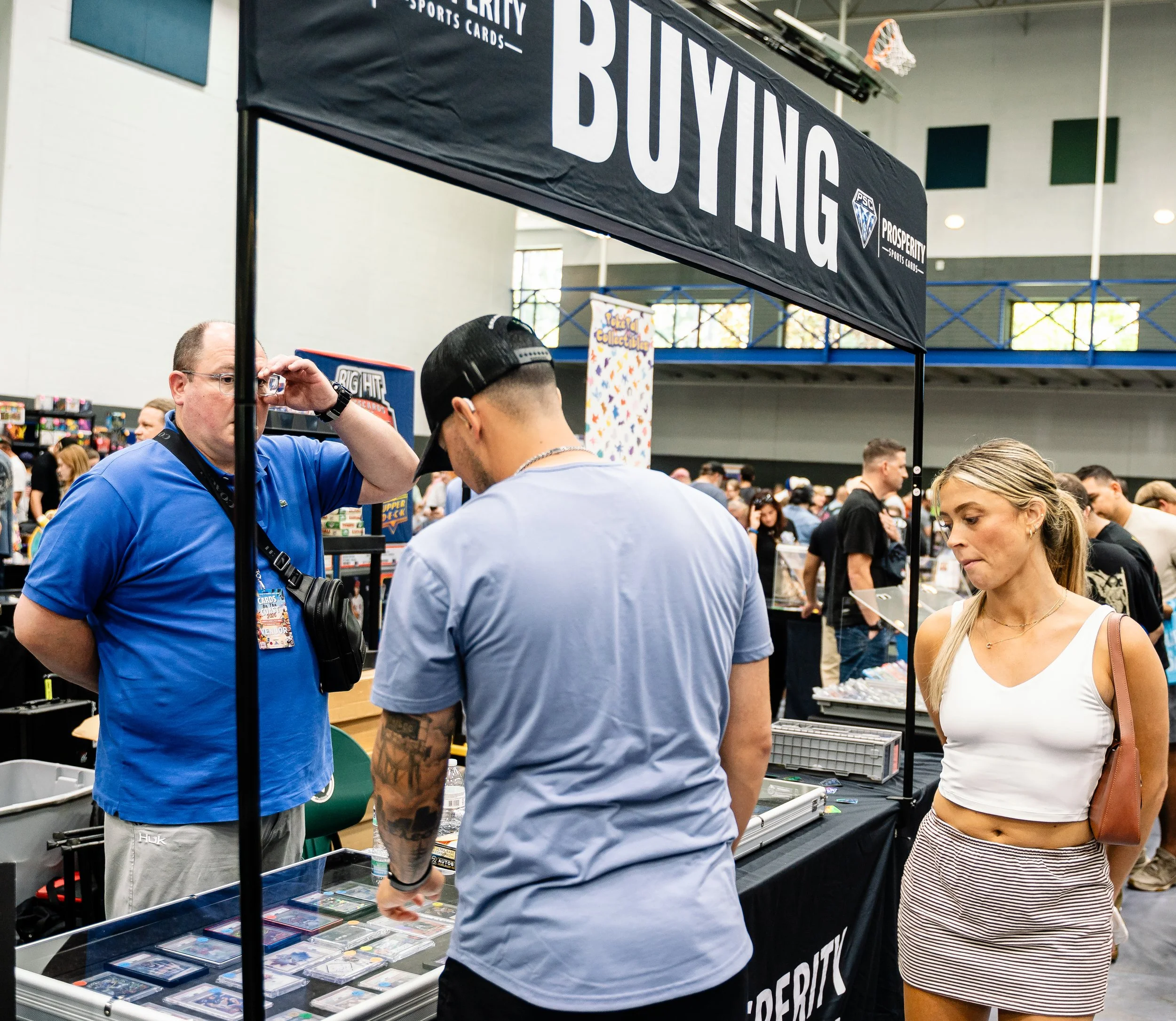 People browsing sports cards at a vendor booth labeled "Prosperity Sports Cards" in a convention center.
