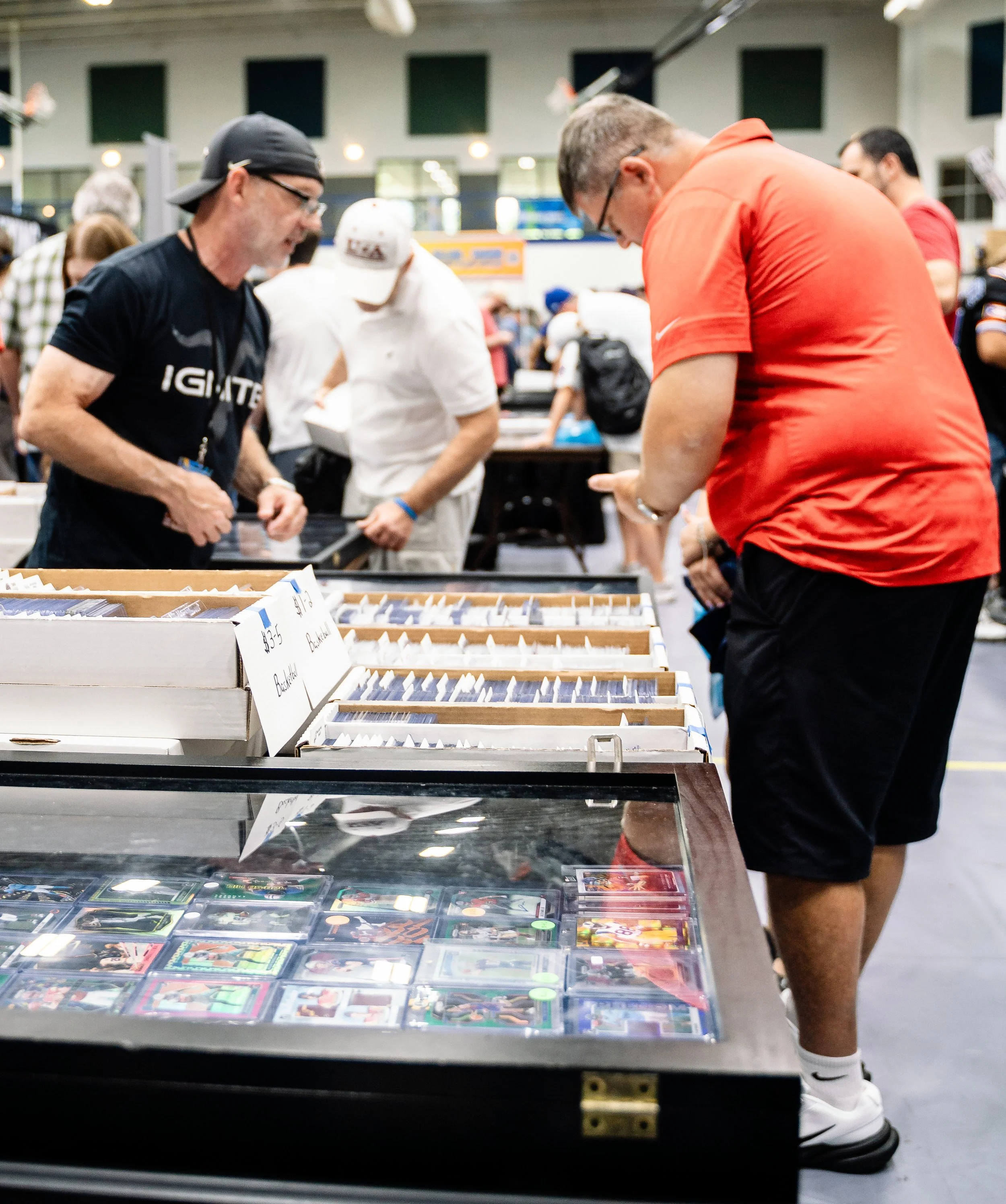 People browsing through a collection of sports cards displayed on a table at a trading card event or store.