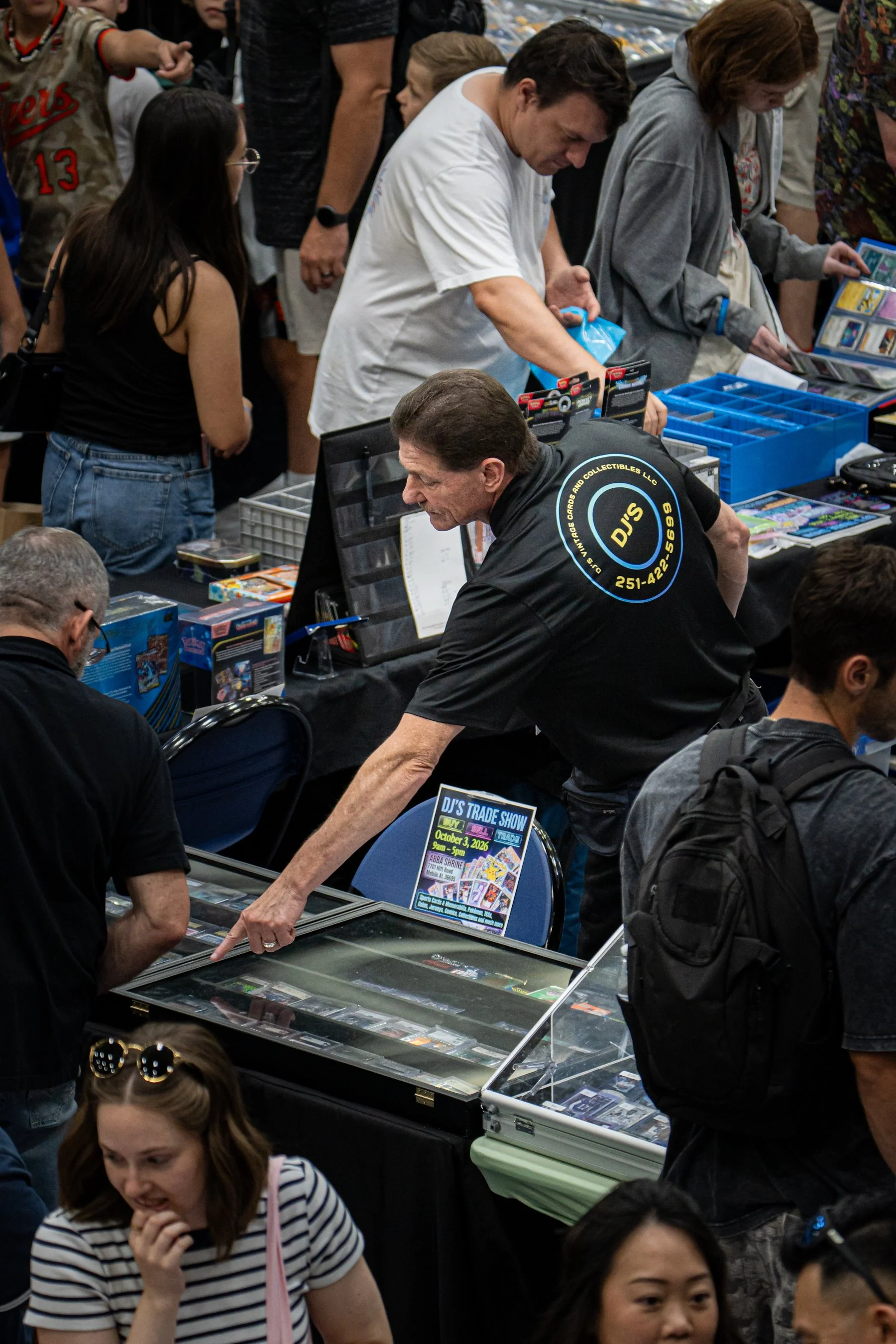 People browsing and purchasing collectibles at a trading card show, with vendor tables displaying cards and merchandise.