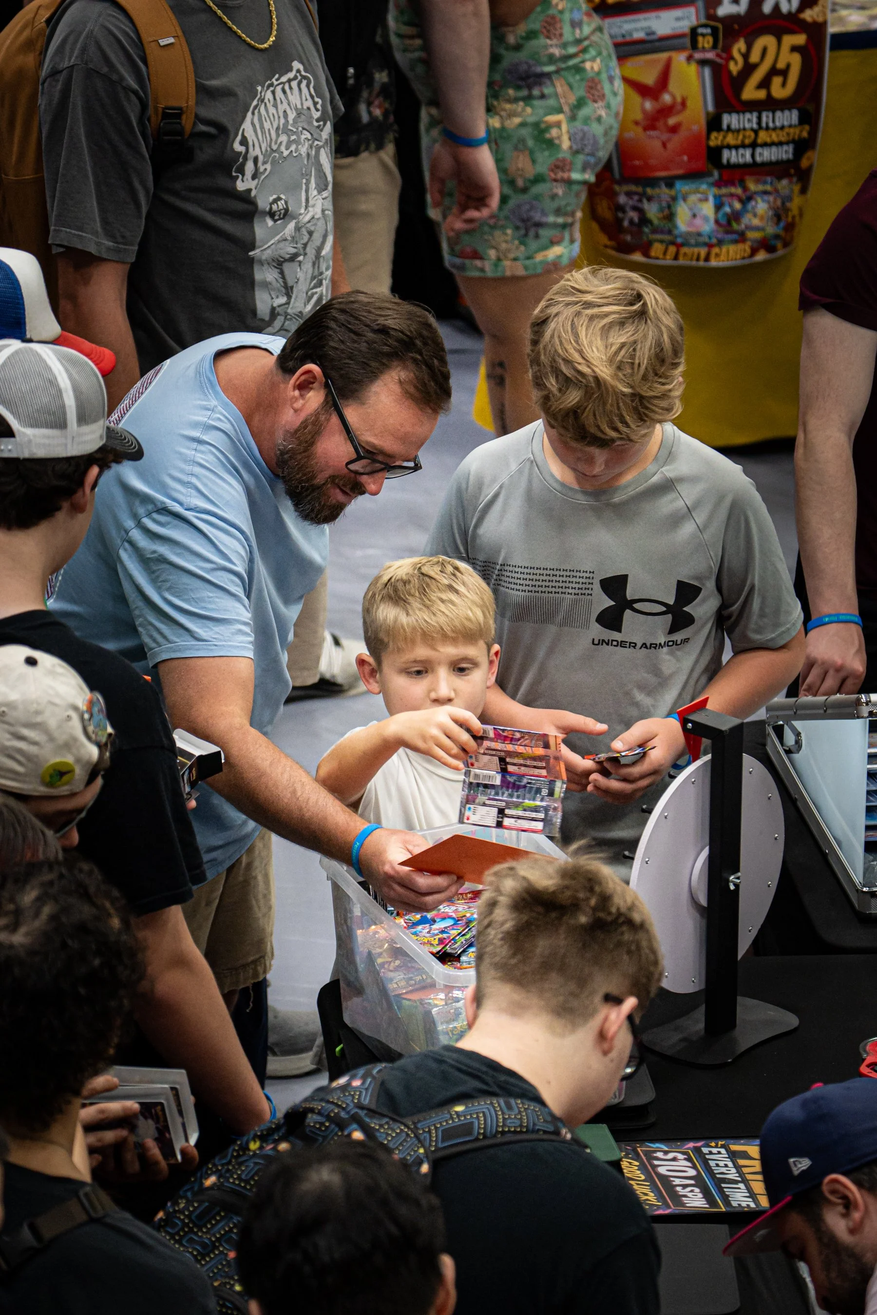 People gathered around a table at a convention, buying and exchanging trading cards and merchandise.