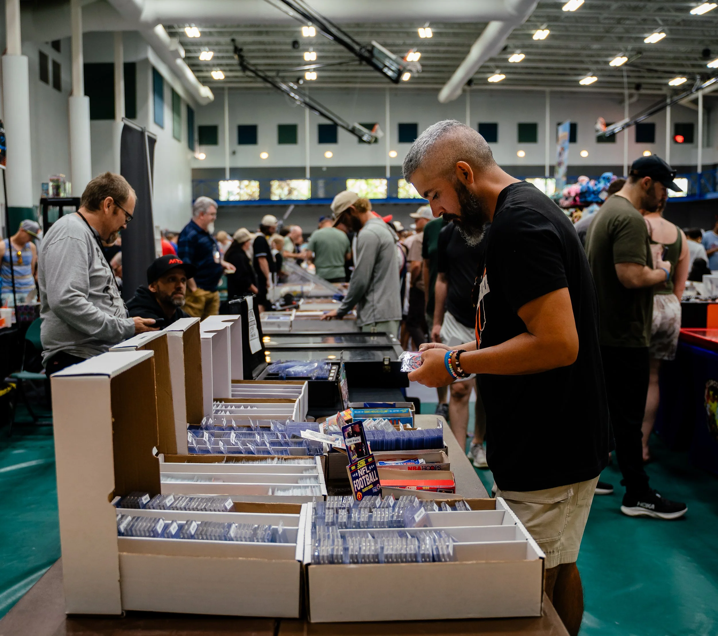 People browsing through books and magazines at a book sale or comic convention in a large indoor venue.