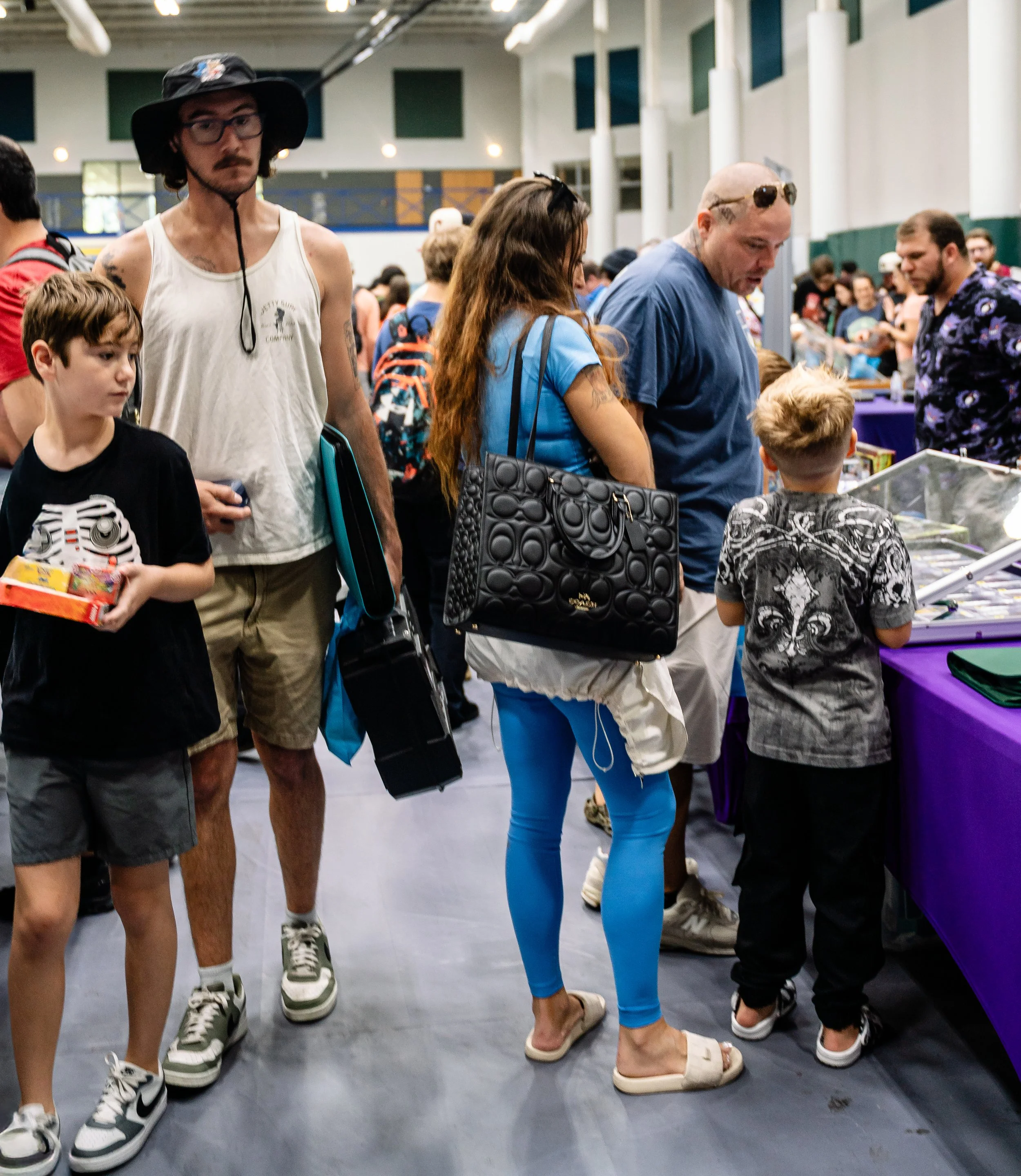 People browsing at an indoor market, with tables displaying items and individuals engaged in shopping.
