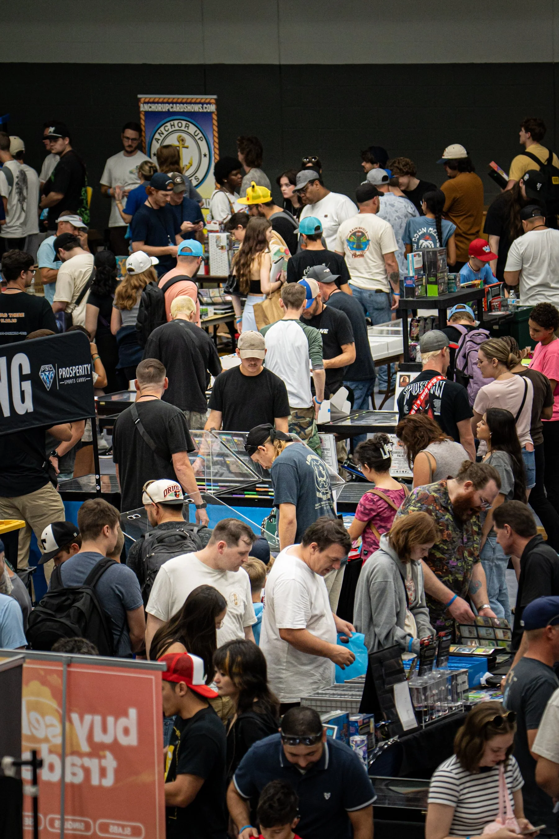 A crowded convention or event with many people browsing tables and booths, with a prominent anchor-themed banner in the background.