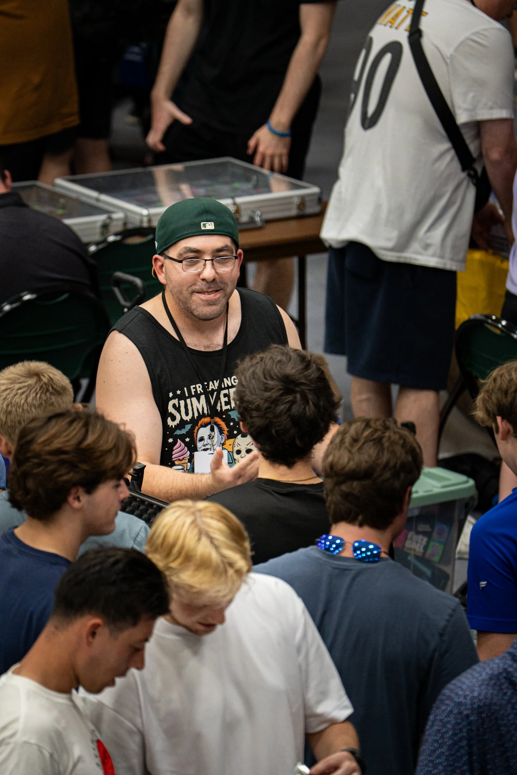 Group of people gathered at a convention or event, some are playing pinball or arcade games, and others are watching or socializing.