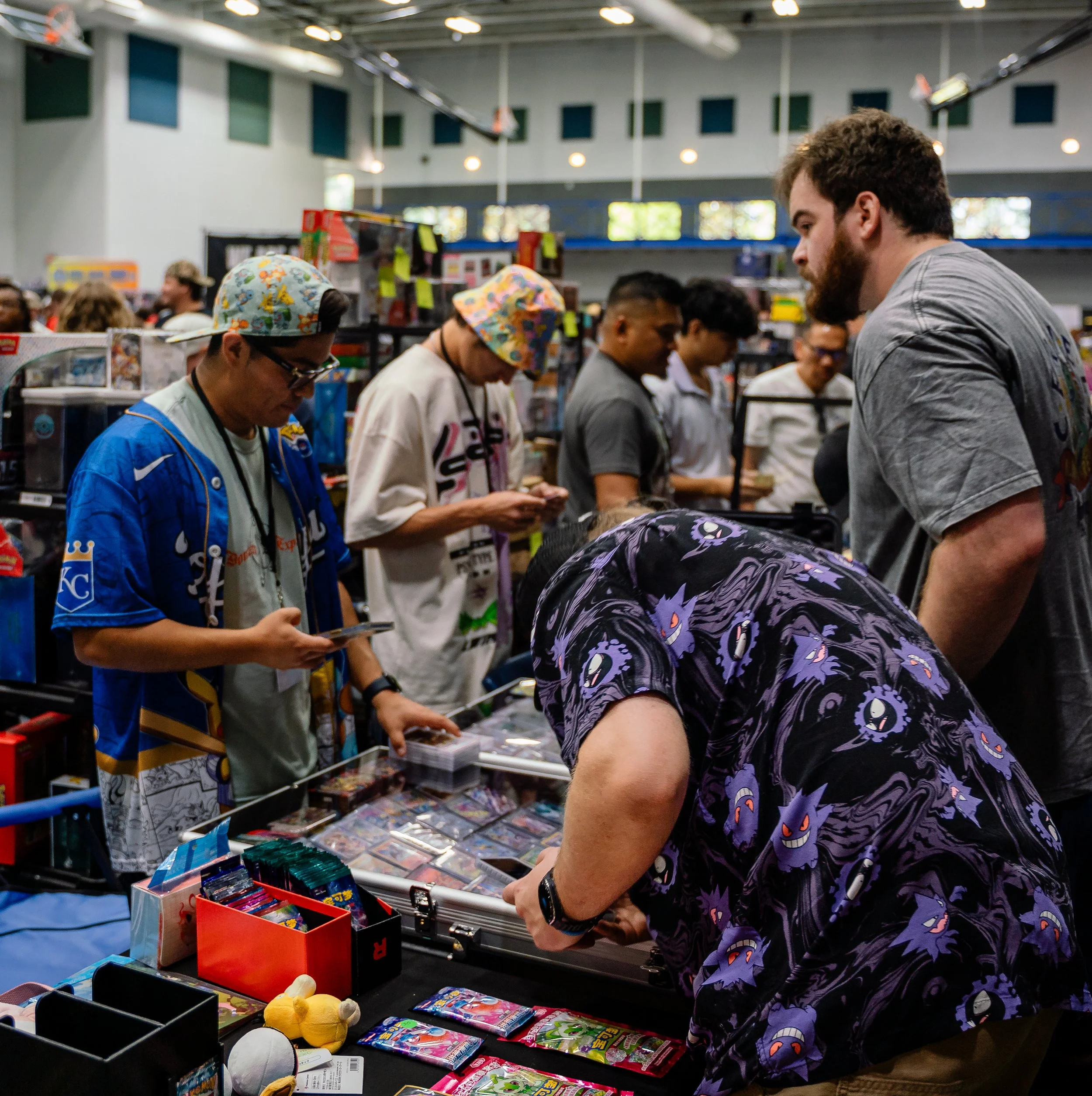 People shopping at a toy store or marketplace with shelves and tables displaying various toys, including plush toys and packaged items. The store has high ceilings and large windows, with shoppers browsing and examining the products.