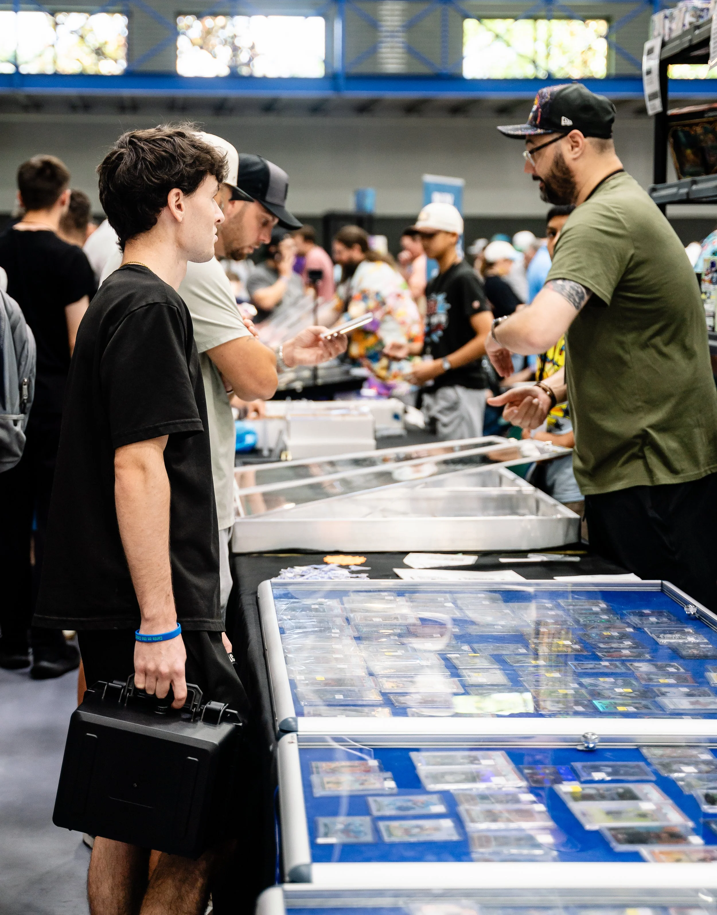 People browsing Pokémon trading cards at a convention or store, with tables displaying various cards.