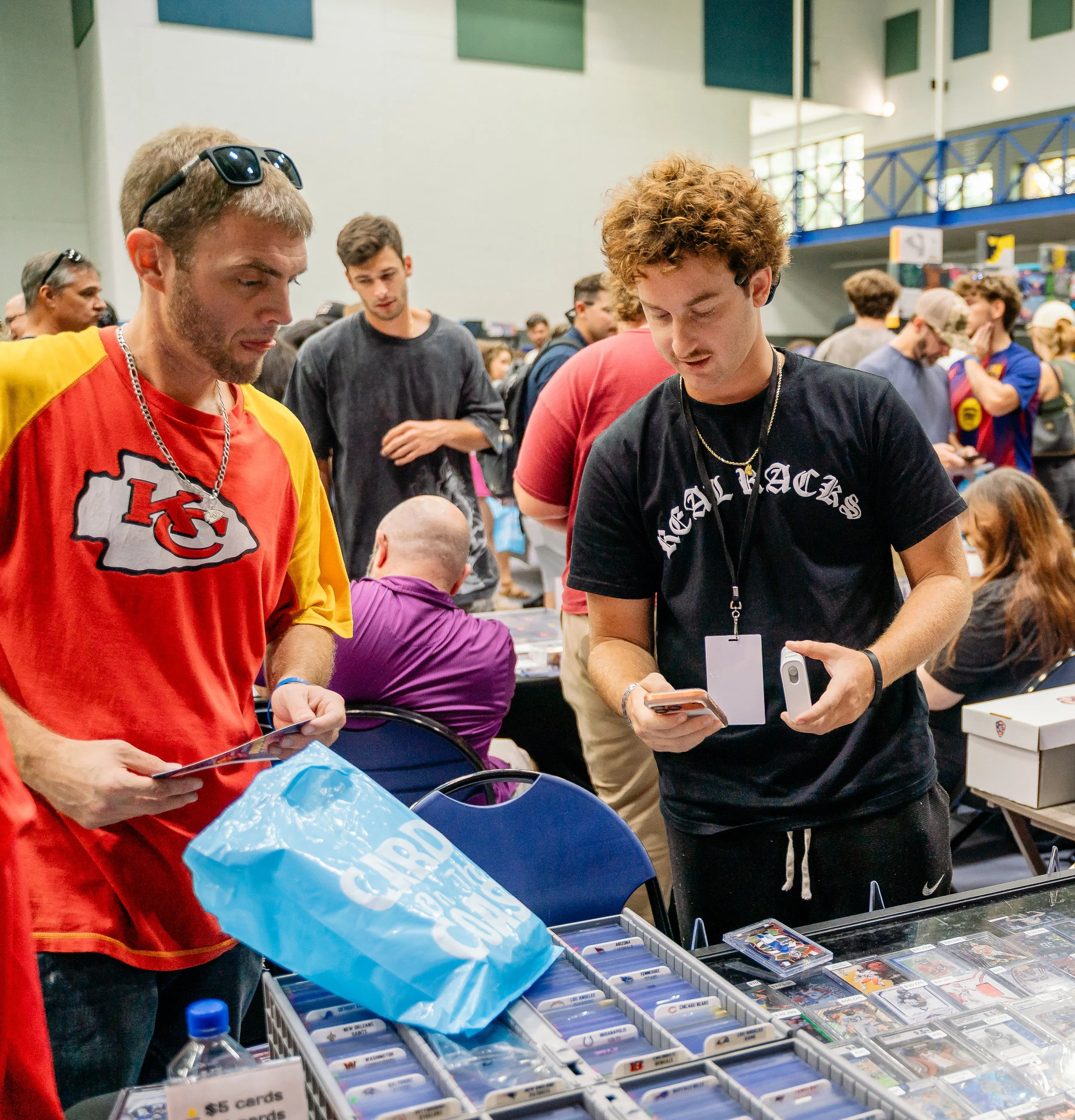 People browsing collectible trading cards at a convention table with organized card storage boxes.