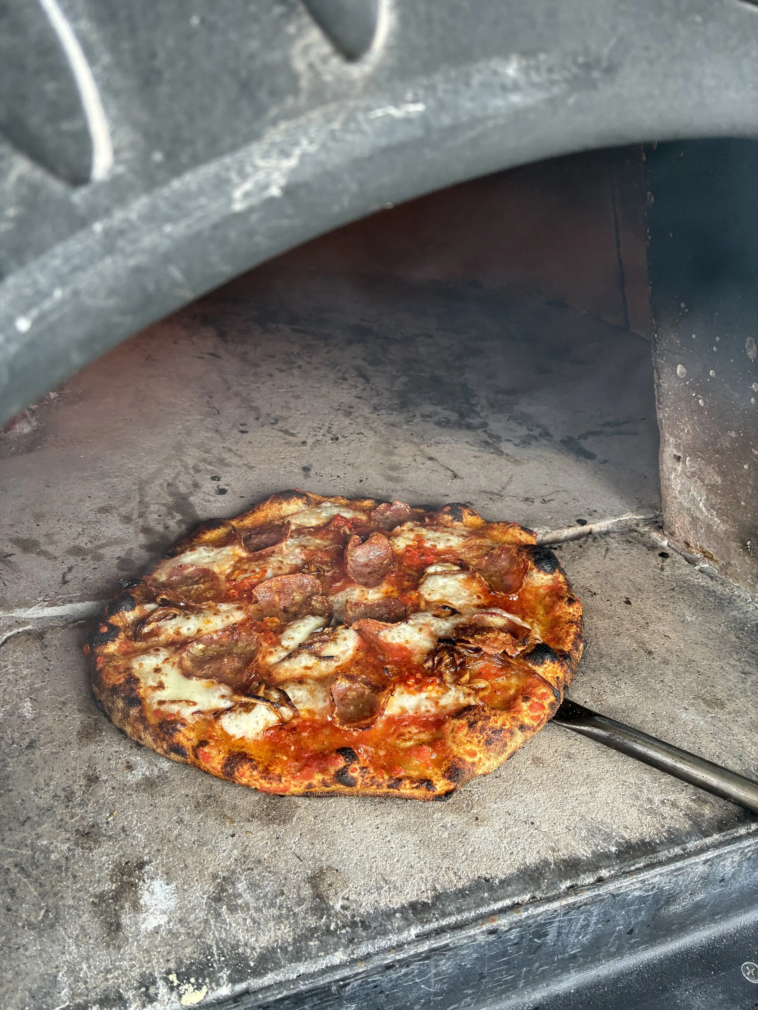 Pizza cooking inside a traditional brick oven, with visible cheese and toppings.