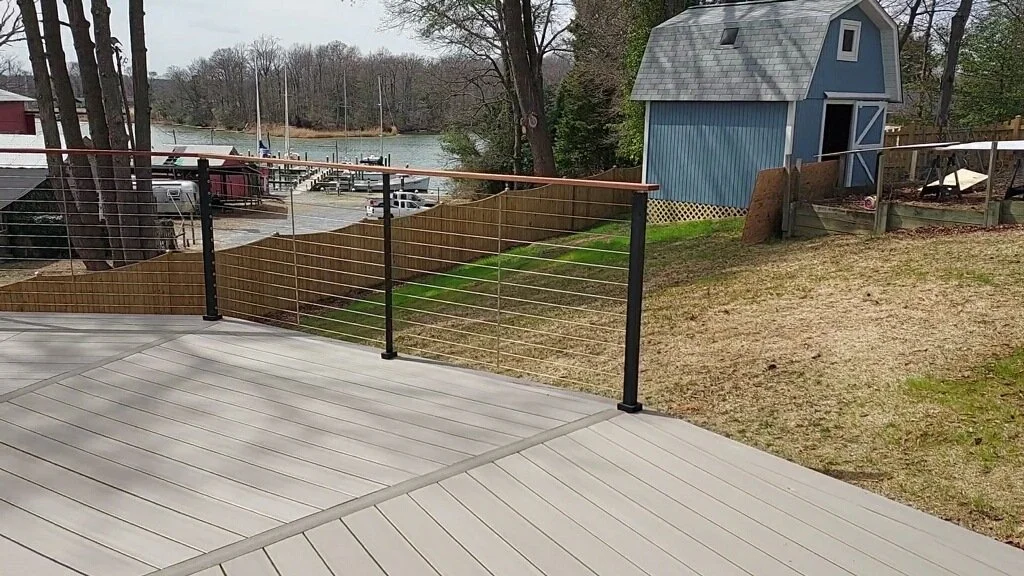 View from a deck overlooking a backyard with a pond, boats, and trees. There is a blue shed and a fenced area.