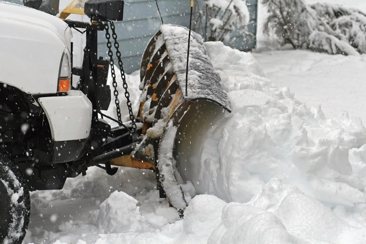 Snowplow clearing snow in a driveway during snowfall.