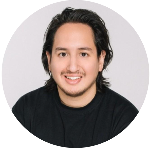 Headshot of a young man with shoulder-length black hair, smiling, wearing a black shirt against a light gray background.