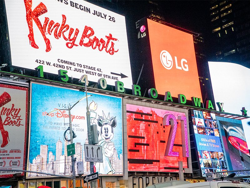 Two men stand in front of a Nasdaq building with a large Nowports advertisement on the digital screen above them.