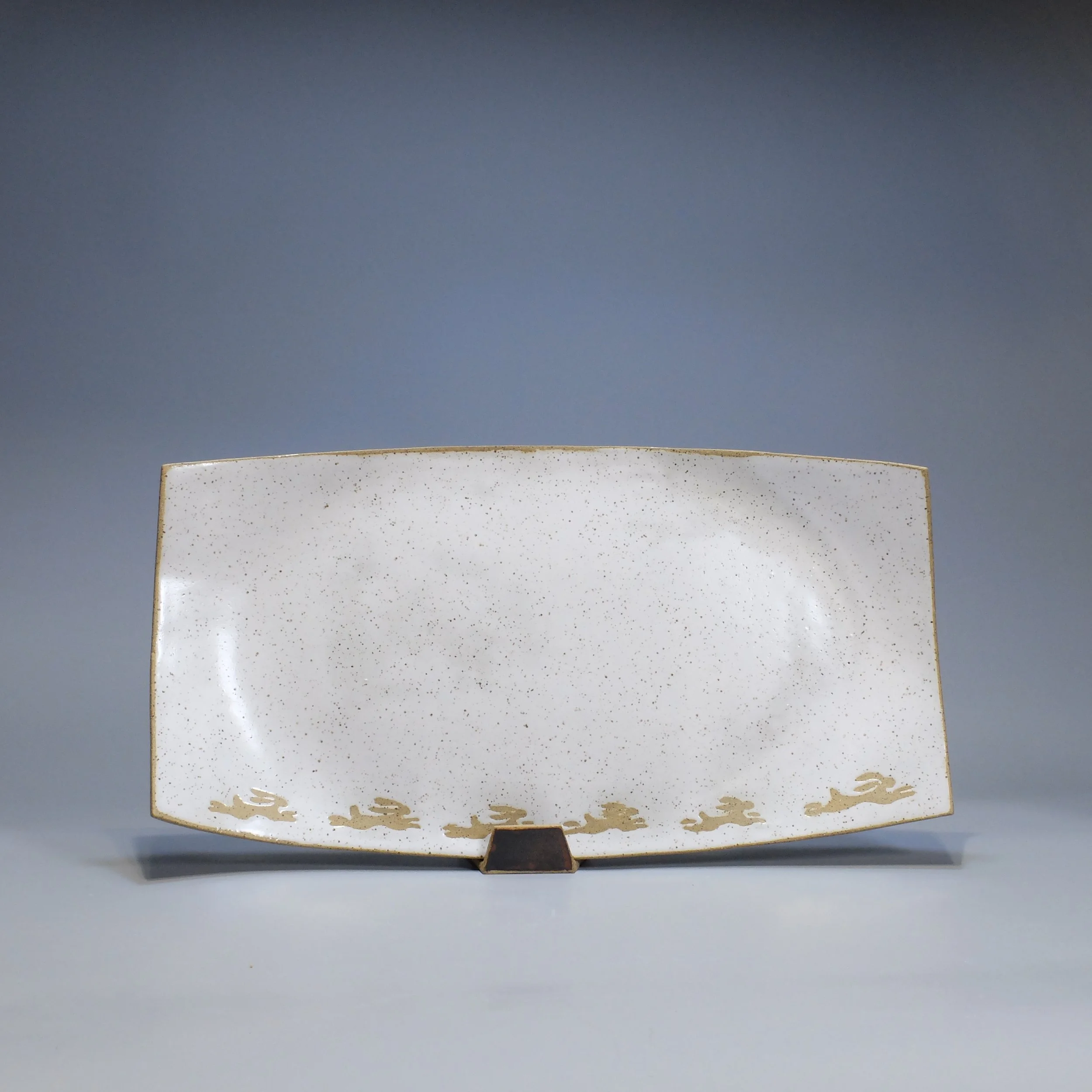 Platter, 2026. Speckled stoneware, white glaze, leaping hare motif. 17.25"L, 8.75"W, 0.75"D.
