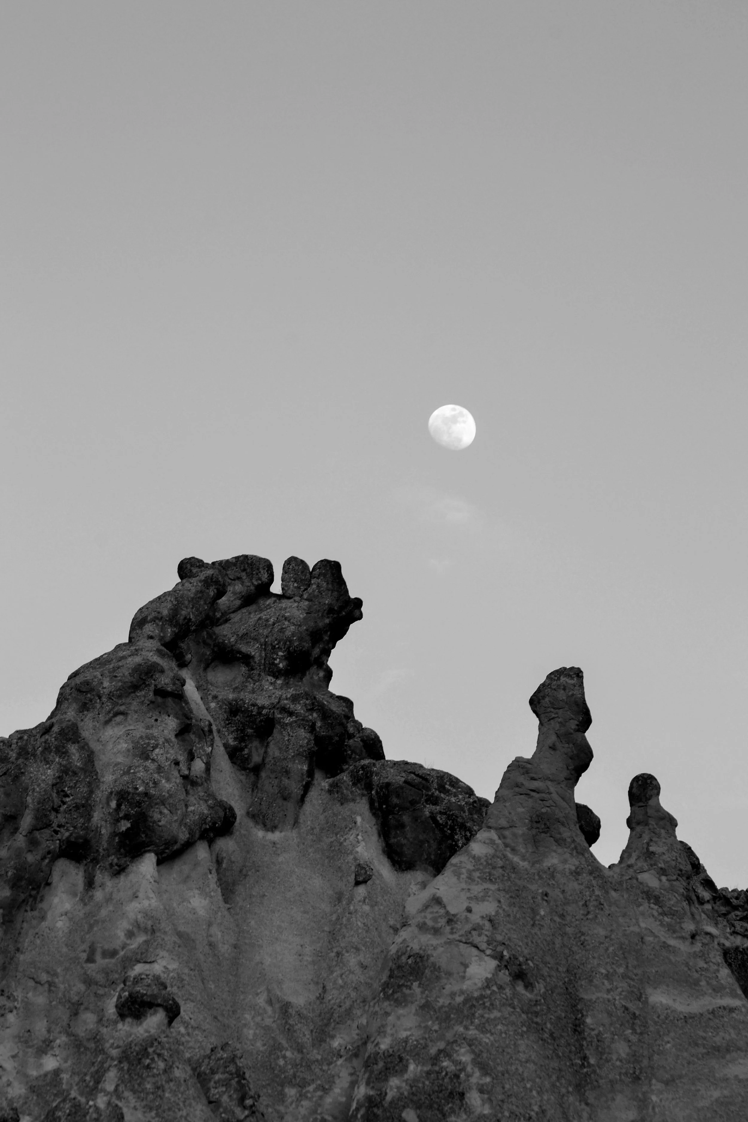 Black and white photo of a rocky landscape with unusual rock formations and the moon high in the sky.