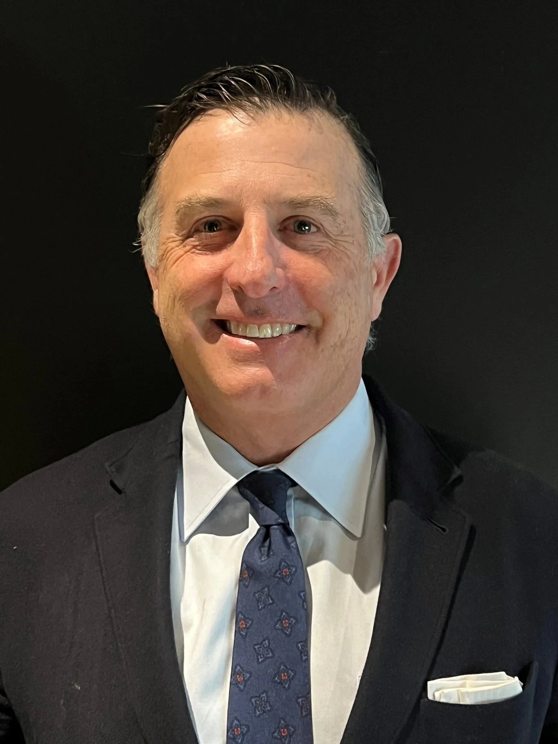 Man smiling in a social setting, with other people in the background.