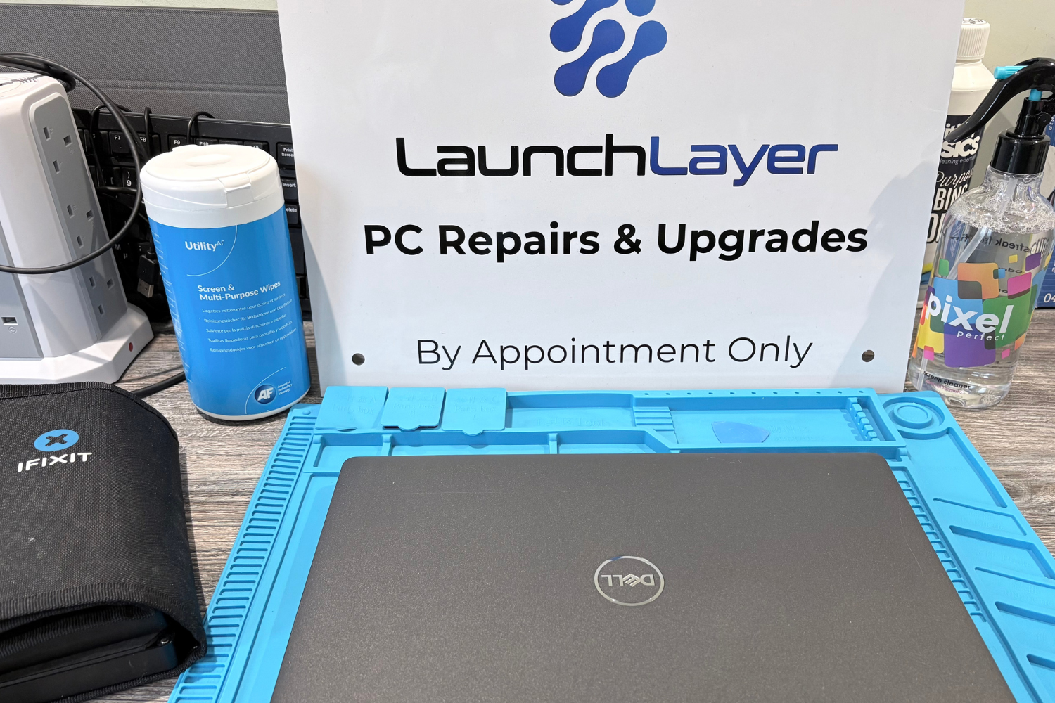 A workspace with a Dell laptop on a blue anti-static mat, a sign for 'LaunchLayer PC Repairs & Upgrades