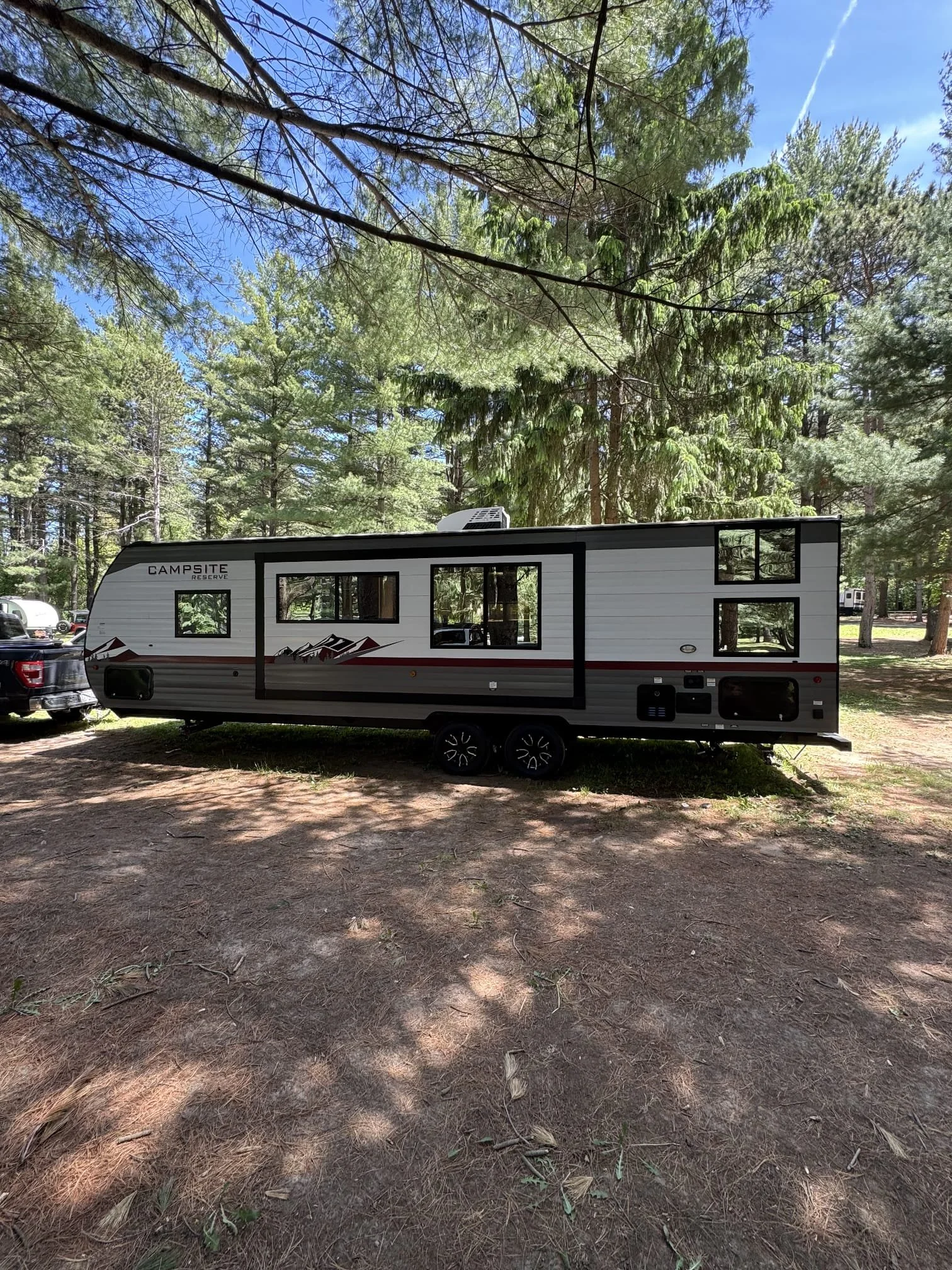 Travel trailer parked on a dirt area surrounded by trees at a campground.
