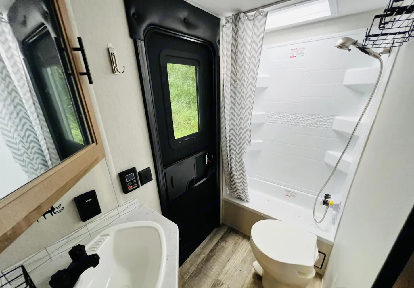 Small bathroom with shower, toilet, sink, mirror, window, and towel curtain in an RV