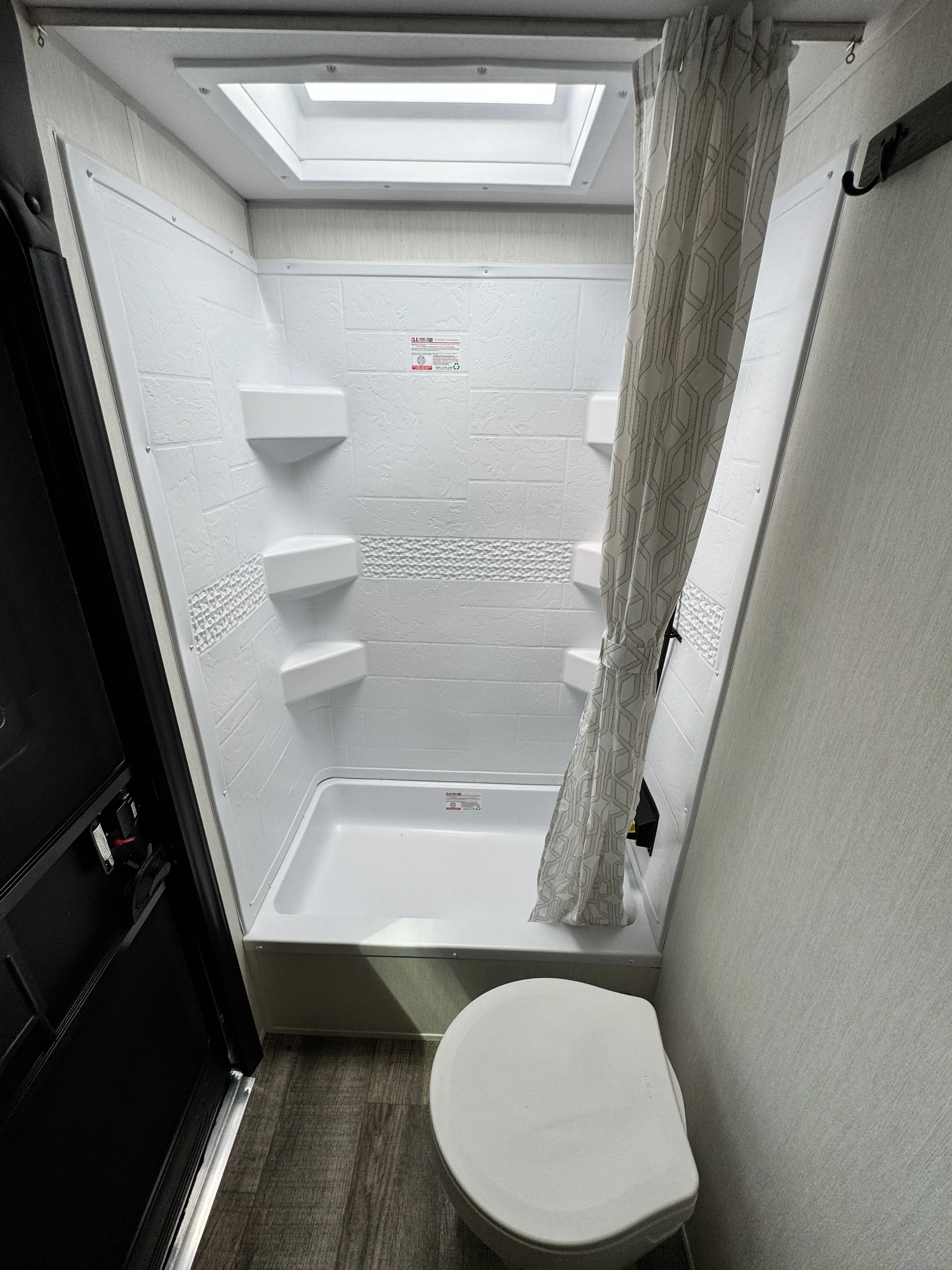 Small bathroom with a shower stall, a curtain, and a toilet. The shower has built-in shelves and a skylight above.
