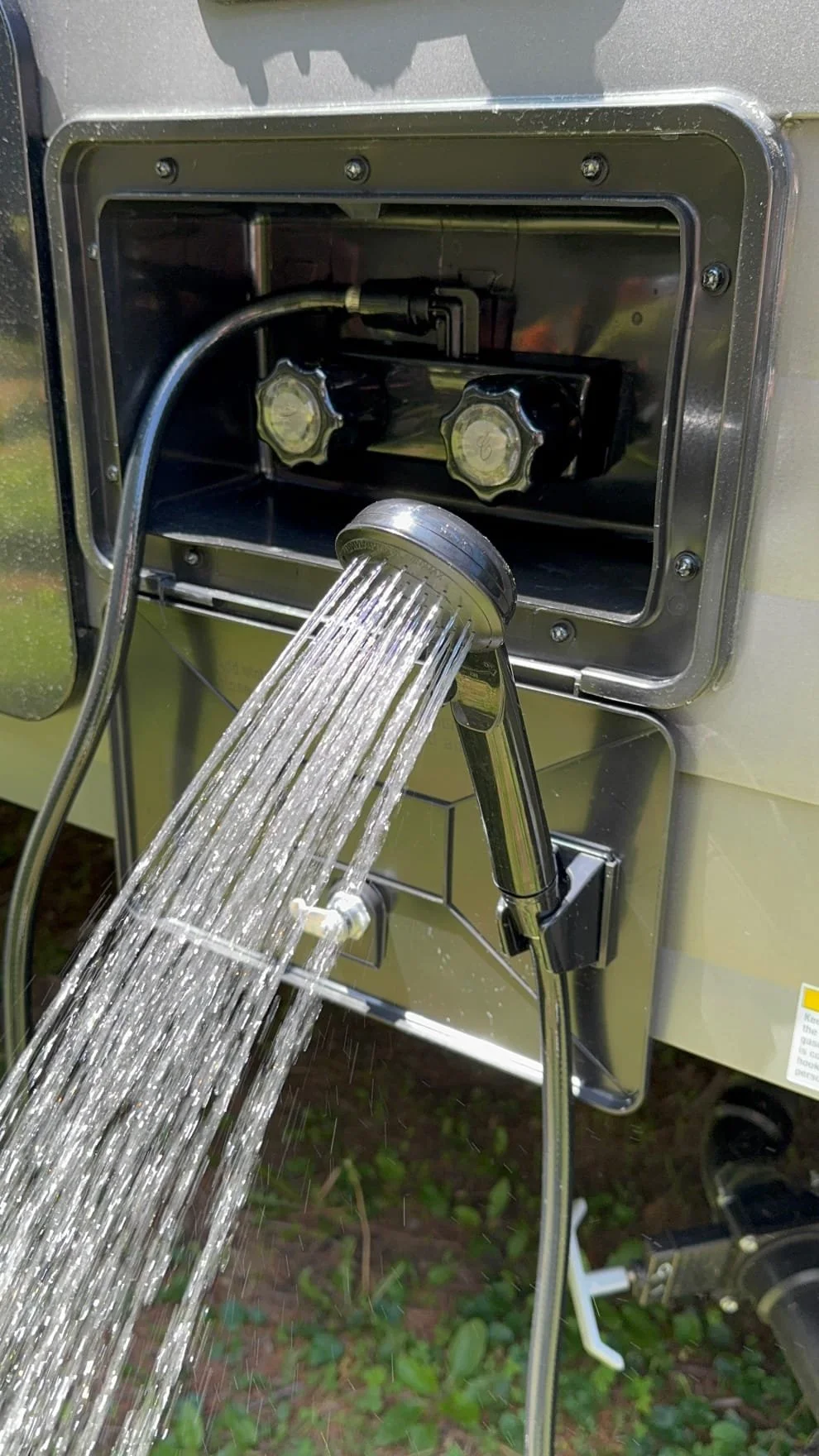 A close-up view of an outdoor shower system connected to a water supply, with water flowing from the showerhead.