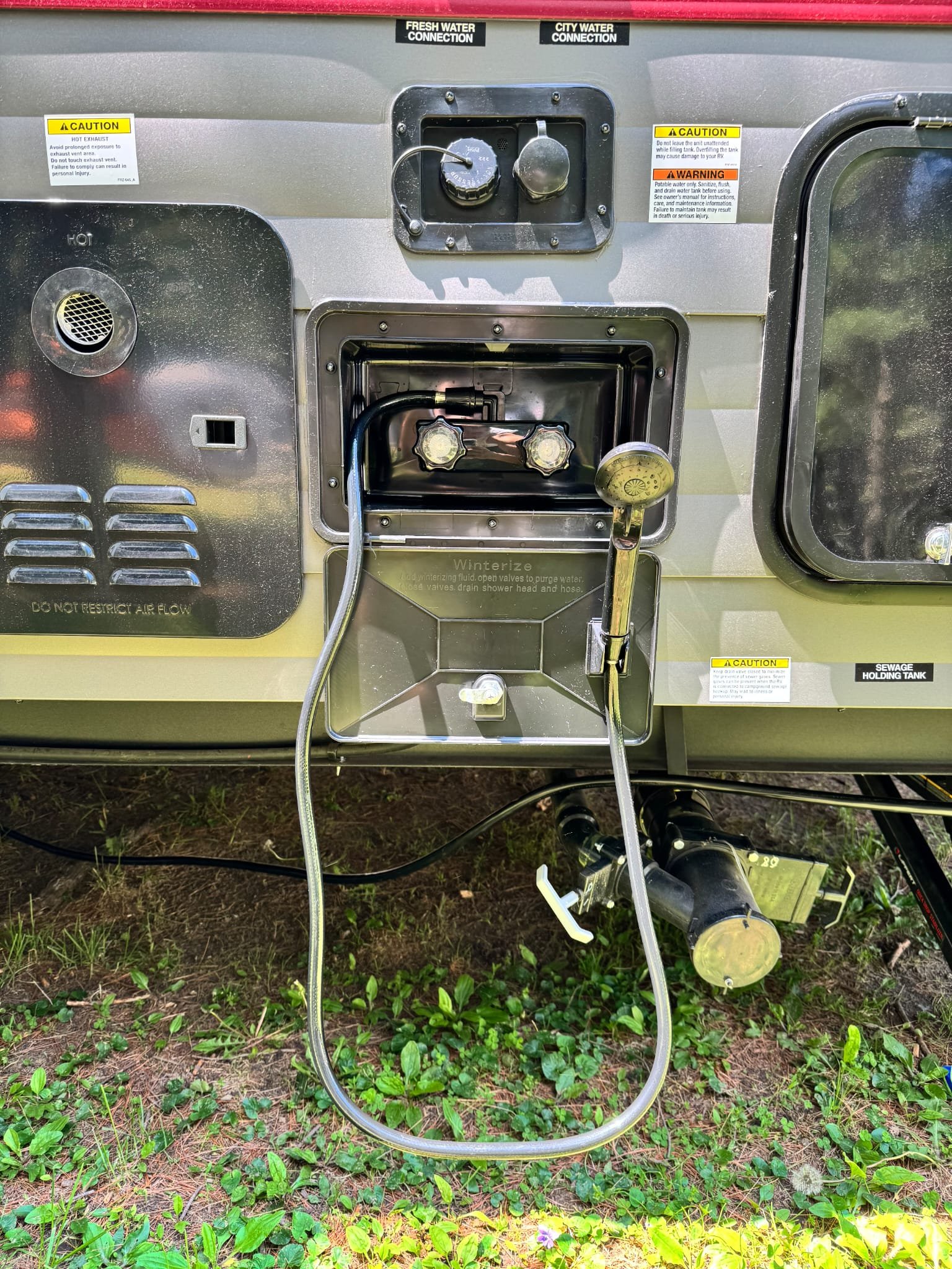 Close-up of a portable water station with hoses and control knobs, set on grassy ground.