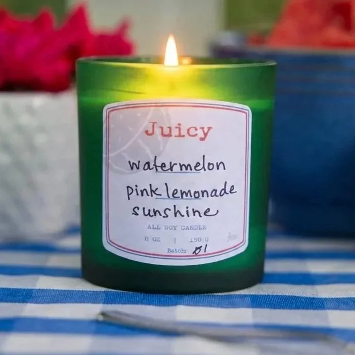 Aeris Juicy candle in green glass jar with handwritten label, styled with watermelon and a wooden lid.