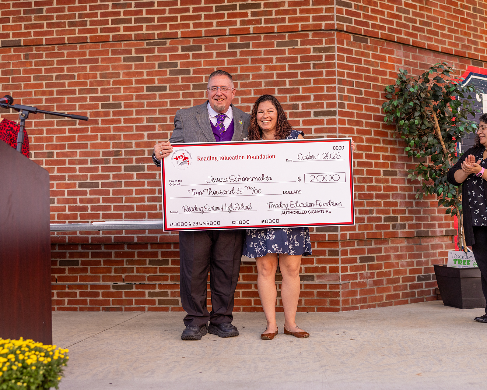 Jessica Schoonmaker holding a giant check from Reading Education Foundation for her teacher grant in front of a brick background
