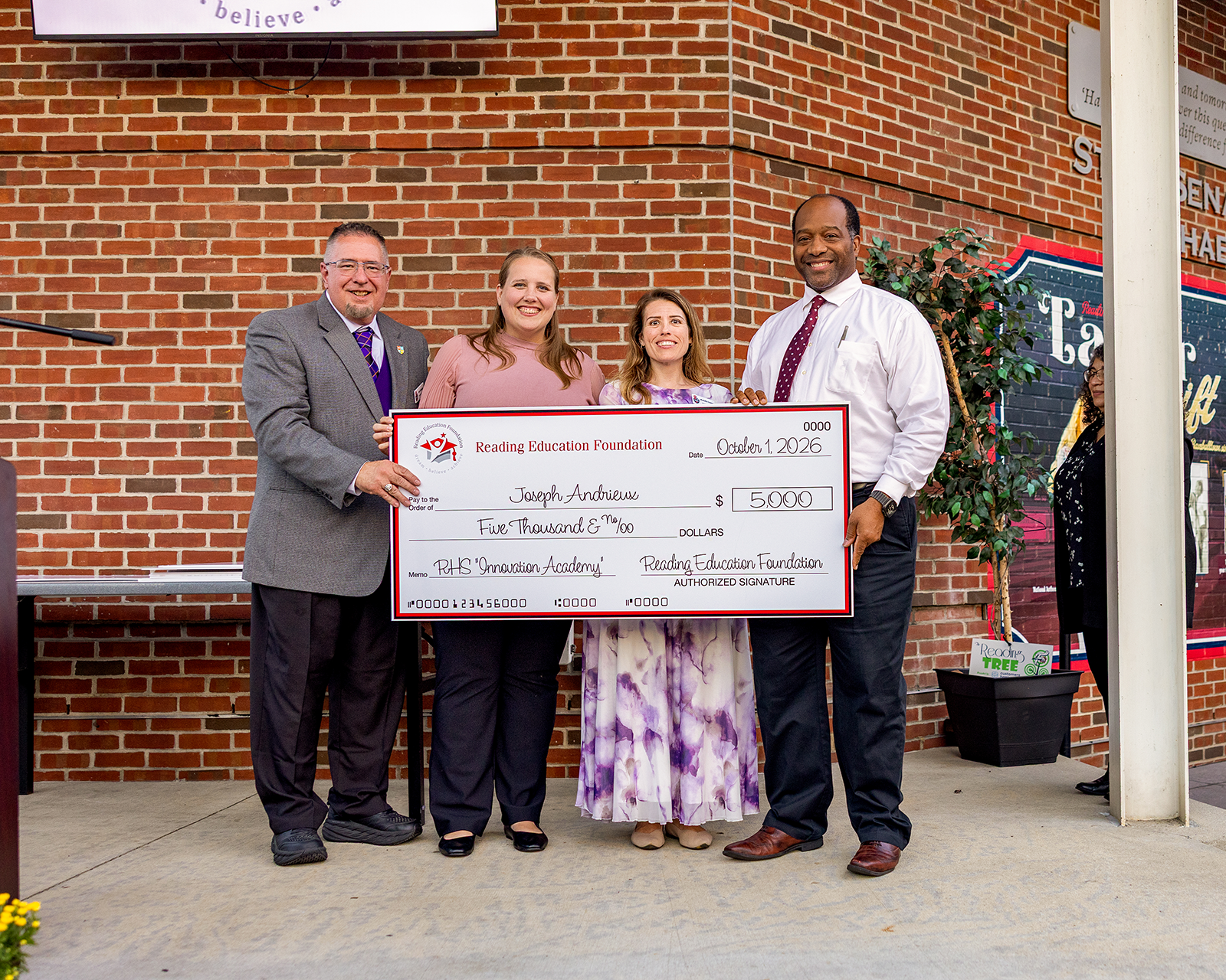 Joseph Andrieux holding a large check from Reading Education Foundation in front of a brick background