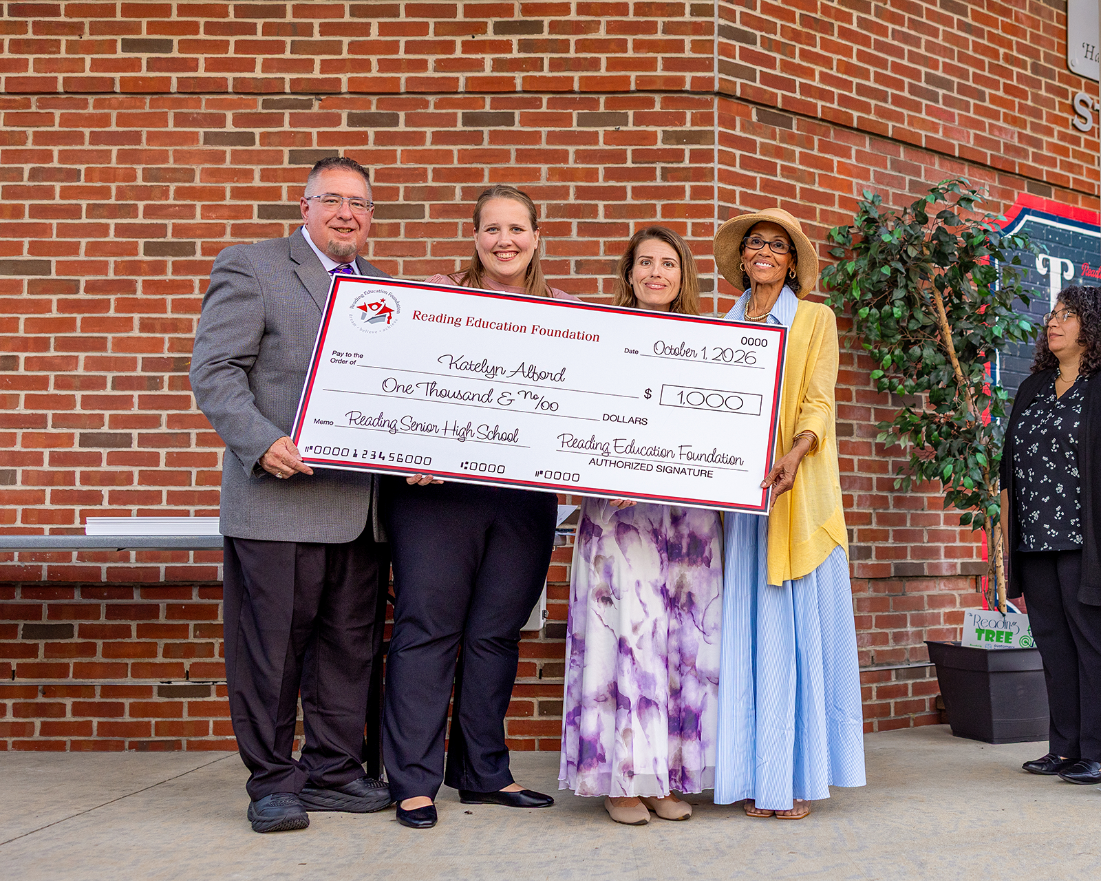 Katelyn Alford holding a large check from the Reading Education Foundation for her teacher grant in front of a brick wall.