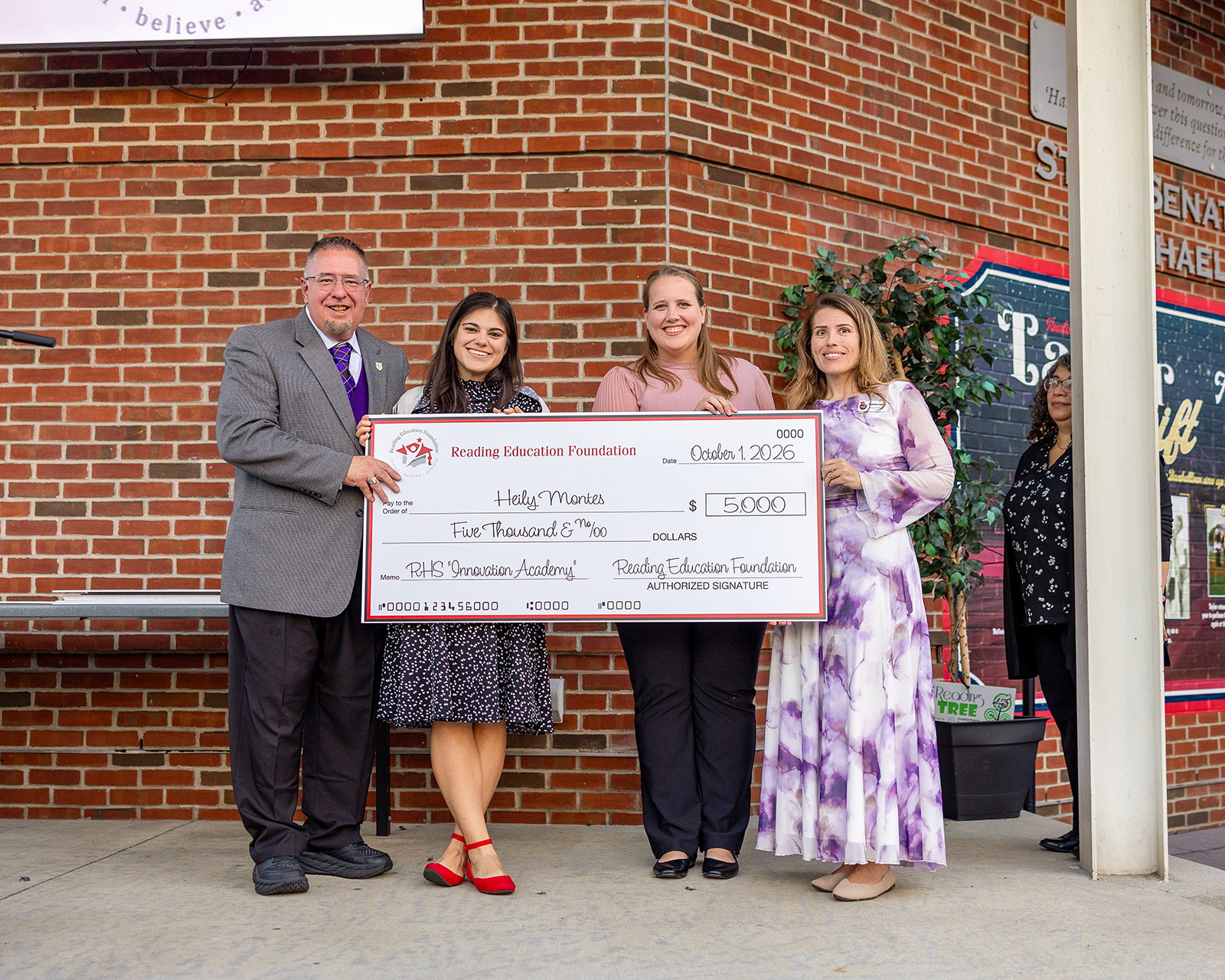 Heily Montes holding a big check from Reading Education Foundation in front of a brick background