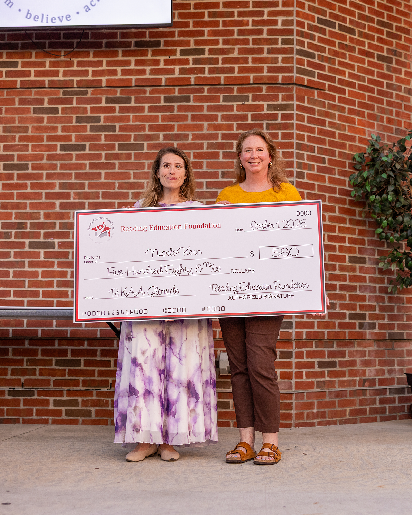Nicole Kern holding her large grant check from Reading Education Foundation in front of a brick wall.